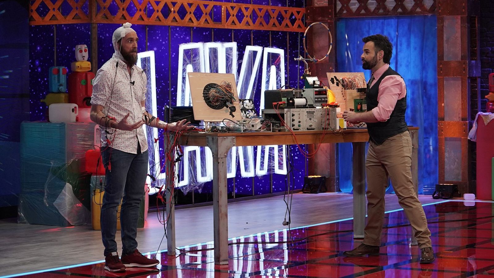 Eduardo Sáenz de Cabezón y Ricardo Moure participan en un experimento científico en el plató de Órbita Laika, junto a una mesa con instrumental y cables.