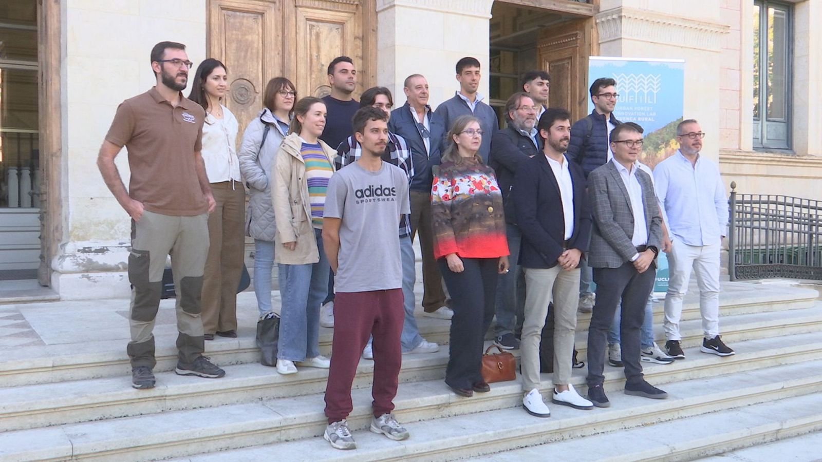 Grupo de quince personas posando en la escalinata de un edificio institucional junto a un cartel del programa UFIL en Cuenca.
