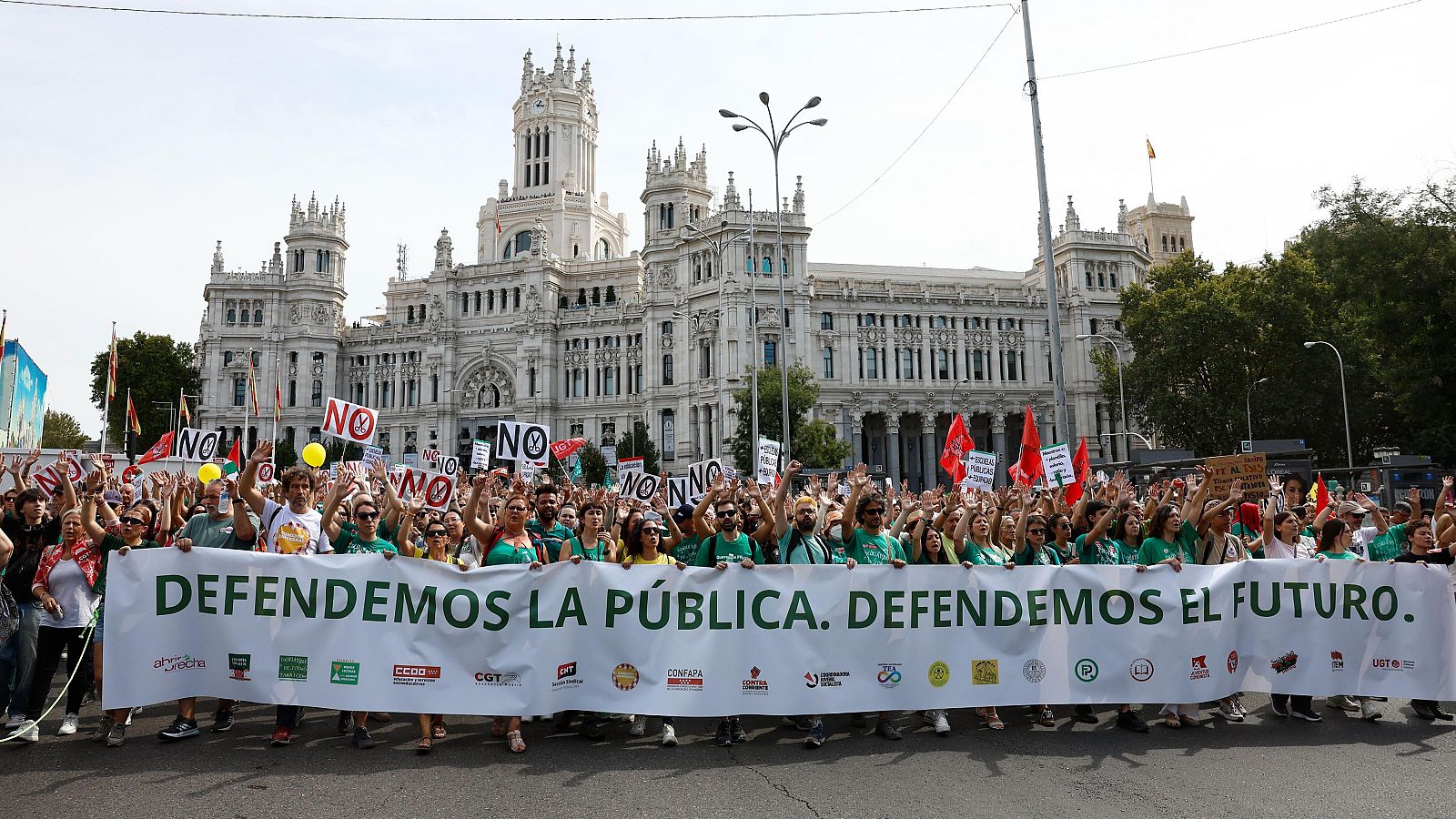 Manifestación en Madrid con una gran pancarta blanca que defiende la educación pública, rodeada de una multitud con camisetas verdes y banderas.