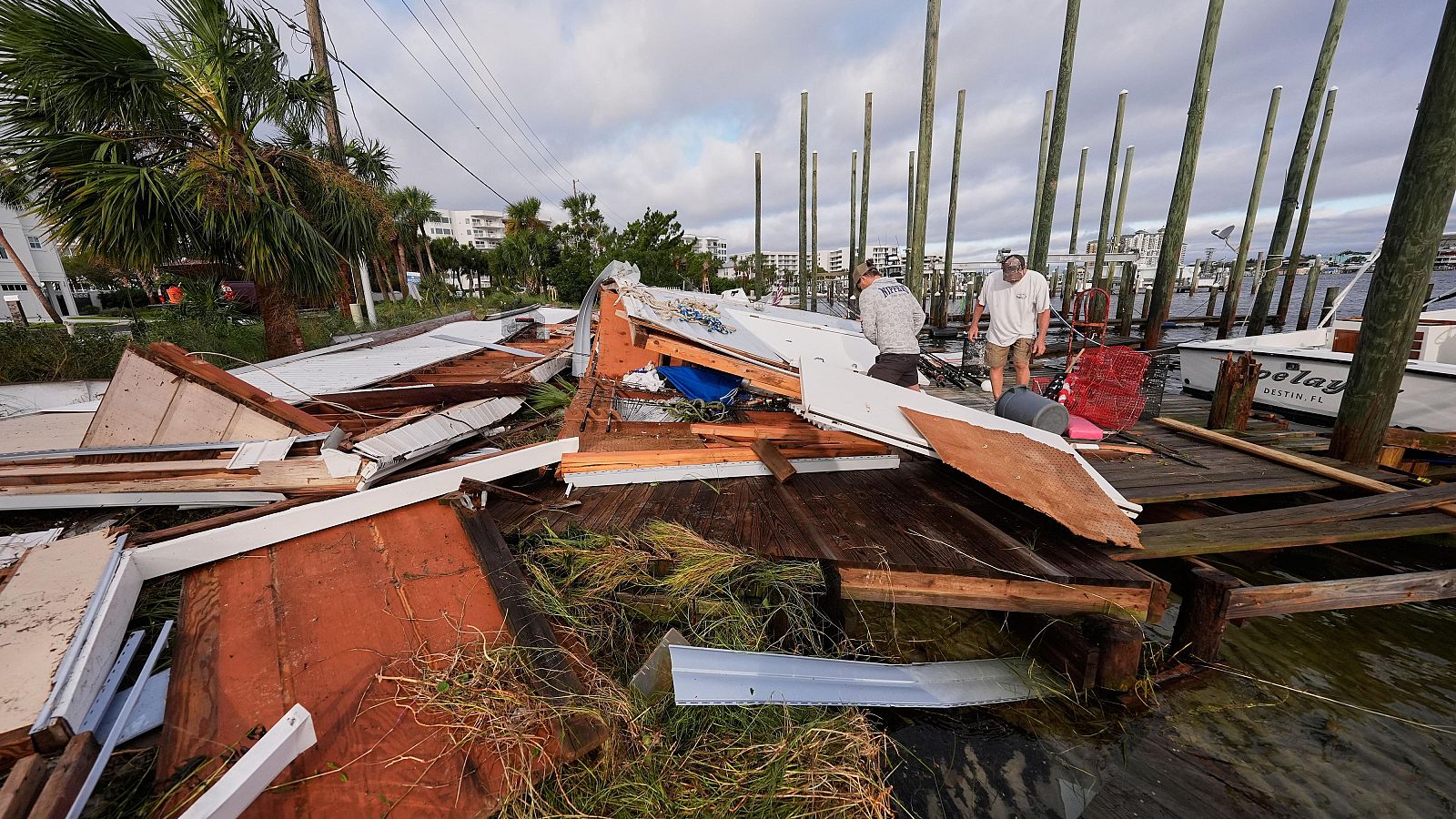 Varias personas recuperan sus pertenencias de un cobertizo para botes derrumbado tras el paso del huracán Isaías en Destin, Florida