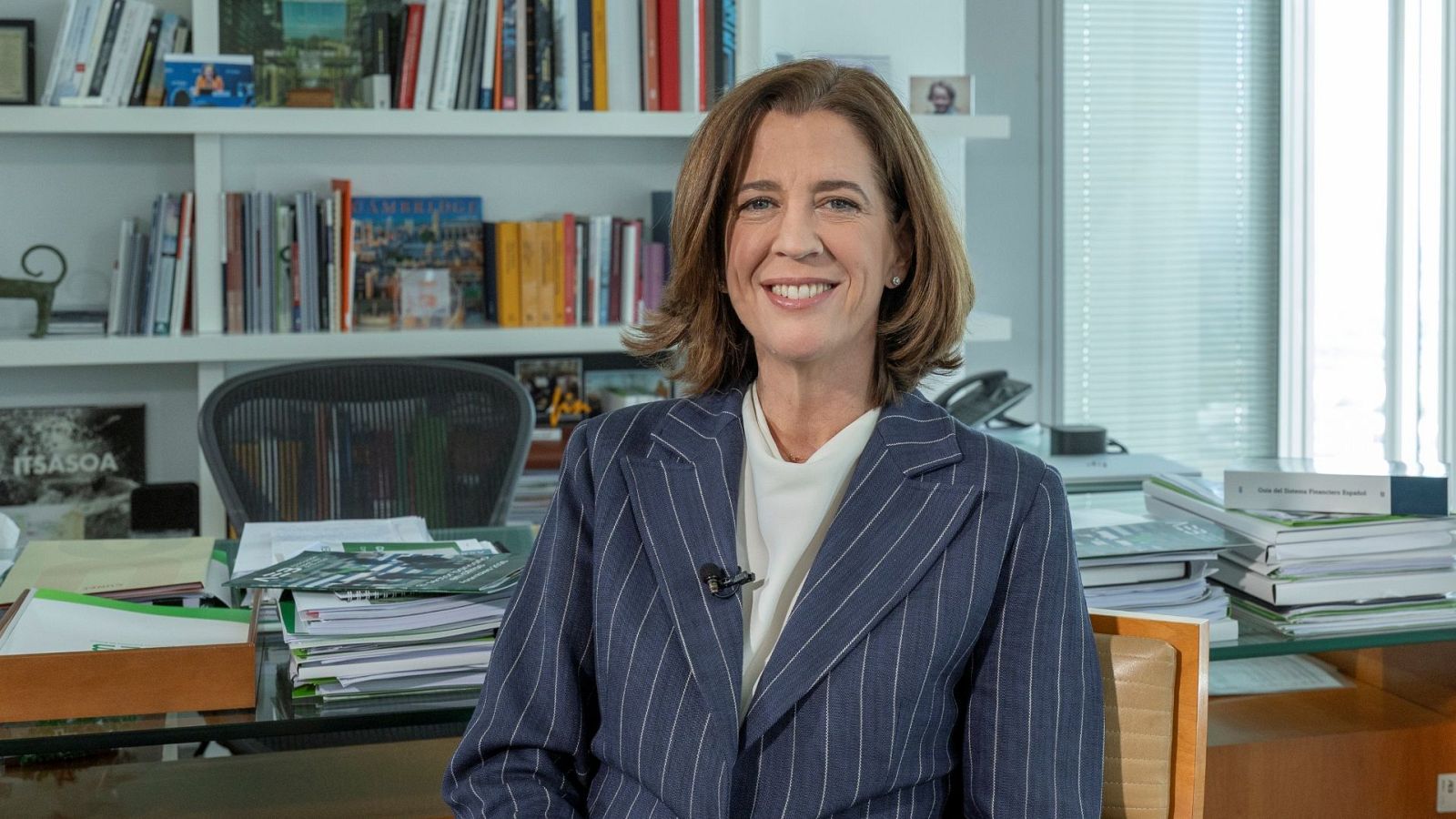 Alejandra Kindelán, presidenta de la AEB, sonríe en su despacho vestida con traje de chaqueta azul marino y blusa marfil en un entorno corporativo.