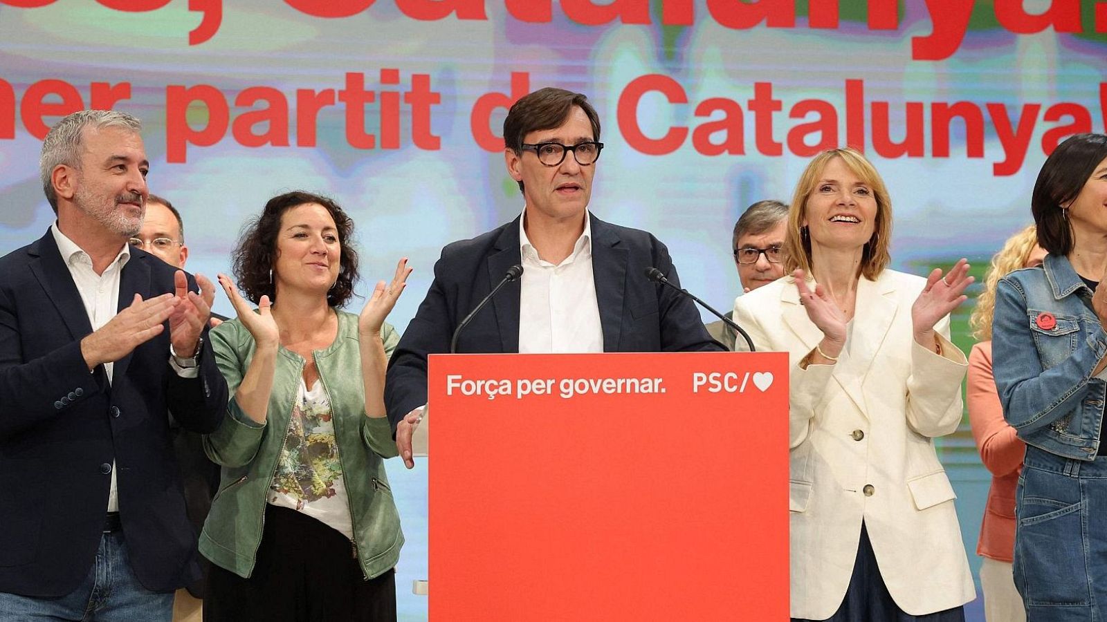 Salvador Illa compareix al costat de membres del PSC davant d'un atril vermell, celebrant la victòria electoral en un ambient de festa.