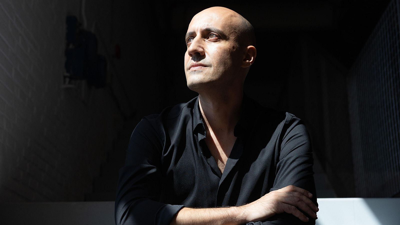 Plano medio del compositor Luis Tabuenca con los brazos cruzados, destacando por un marcado juego de luces y sombras que ilumina diagonalmente su rostro.