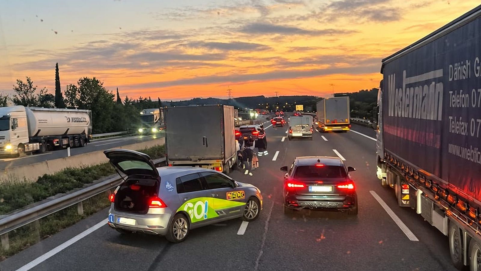 Densa retenció de trànsit a l'autopista al capvespre amb vehicles aturats per un accident i cel ataronjat.