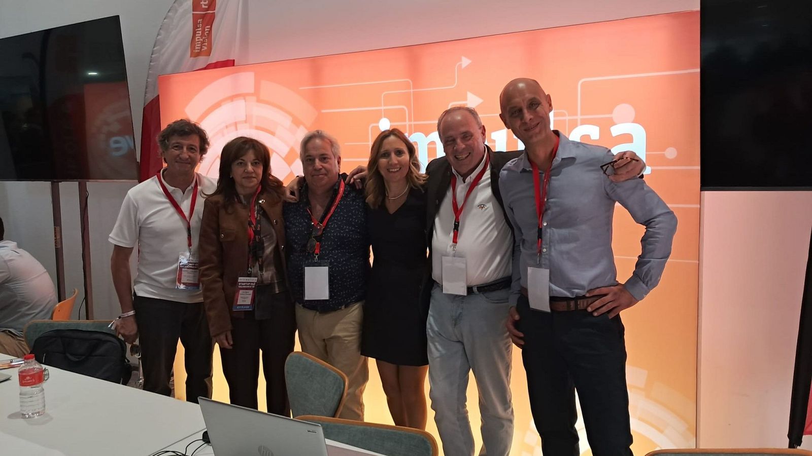 Seis profesionales posan sonrientes y con acreditaciones en un evento corporativo frente a un panel tecnológico naranja con el logotipo de RTVE.
