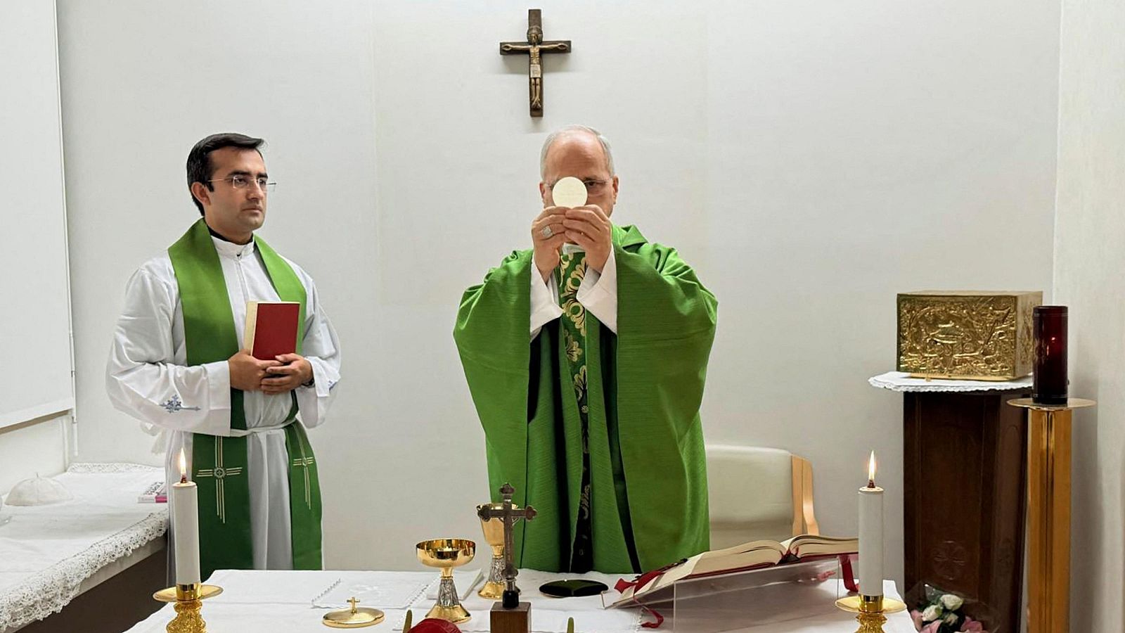 Un sacerdote celebra una misa en una capilla, elevando la hostia consagrada en el altar.