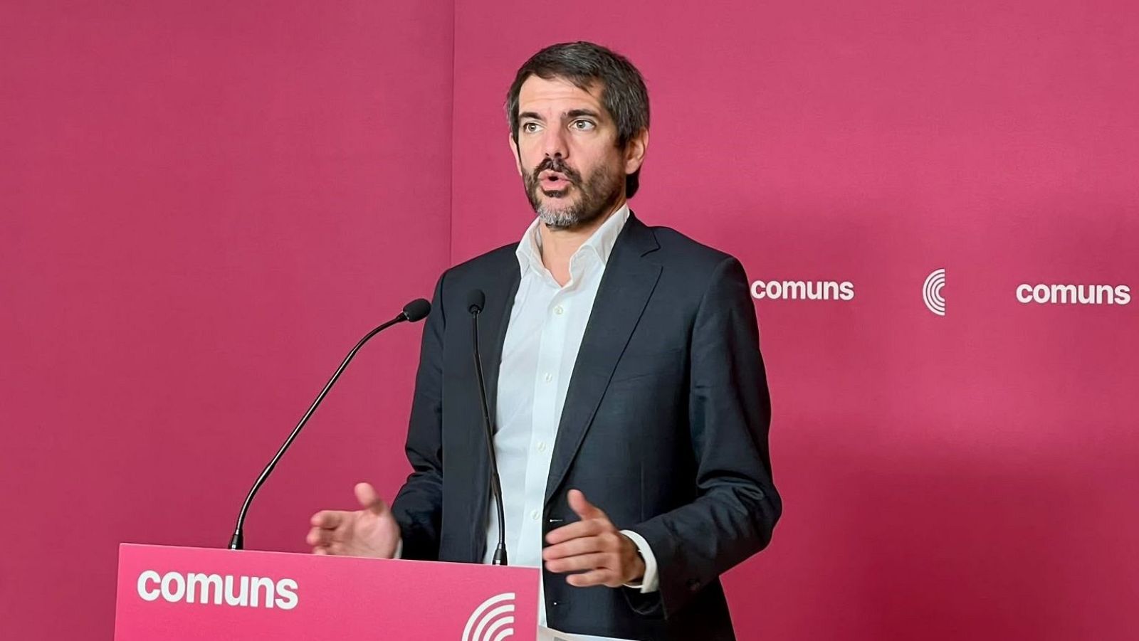 Ernest Urtasun intervé en roda de premsa darrere d'un atril magenta amb el logotip de «comuns».