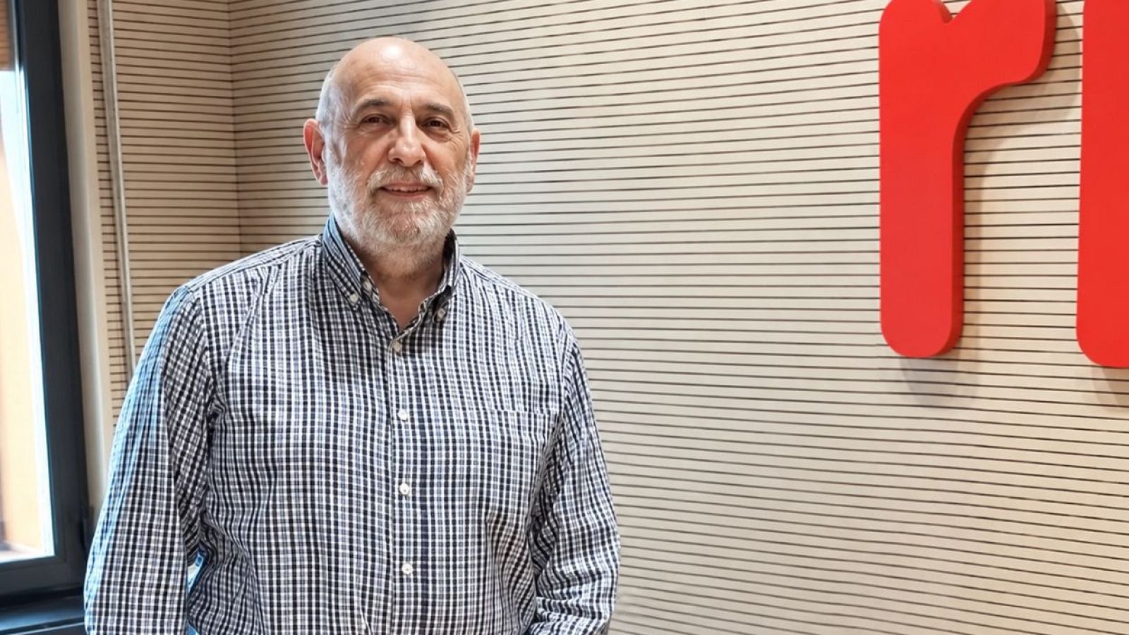 Patxi Tiberio posa sonriente en un estudio de radio con paneles acústicos de madera y el logotipo de RNE al fondo.