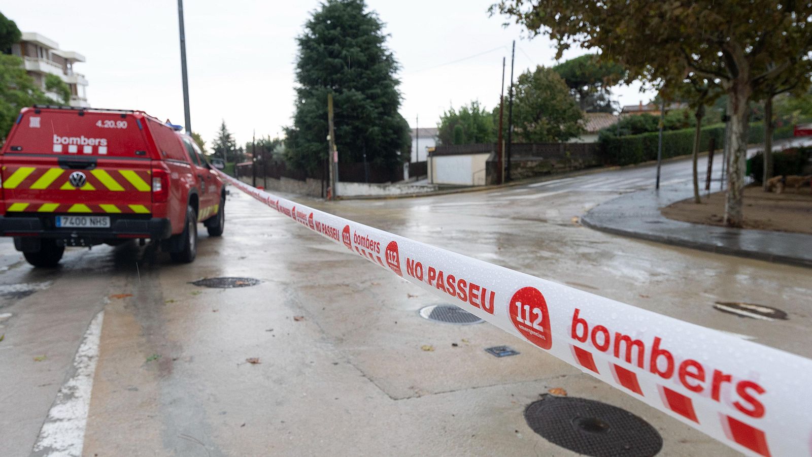 Carrer tallat pels bombers amb cinta de balizament i una camioneta vermella sobre asfalt mullat un dia nublat.