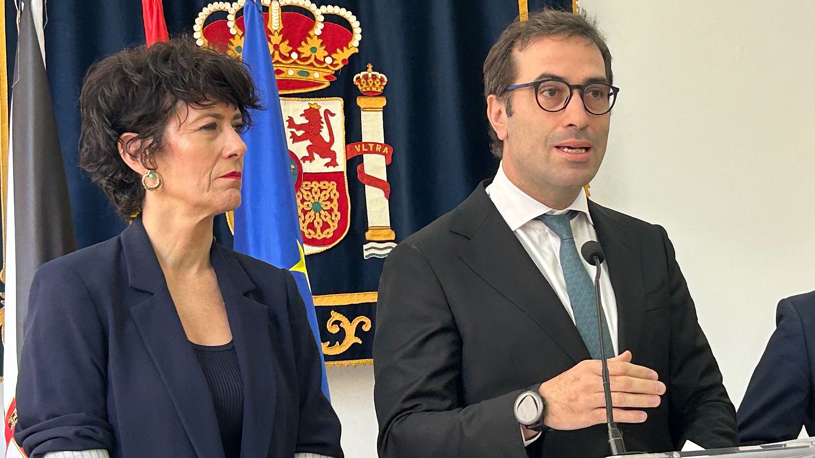 Carlos Cuerpo interviene en una rueda de prensa junto a Elma Saiz ante un tapiz oficial con el escudo de España.