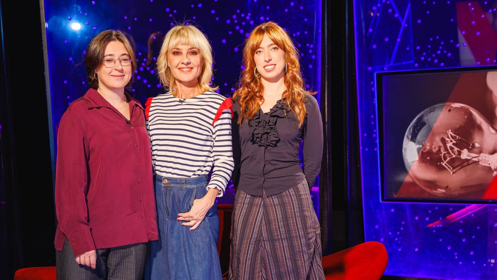 Tres mujeres sonrientes posan en un plató de televisión con fondo azul estrellado, destacando la presentadora en el centro y las dos músicas del grupo Repion a los lados.