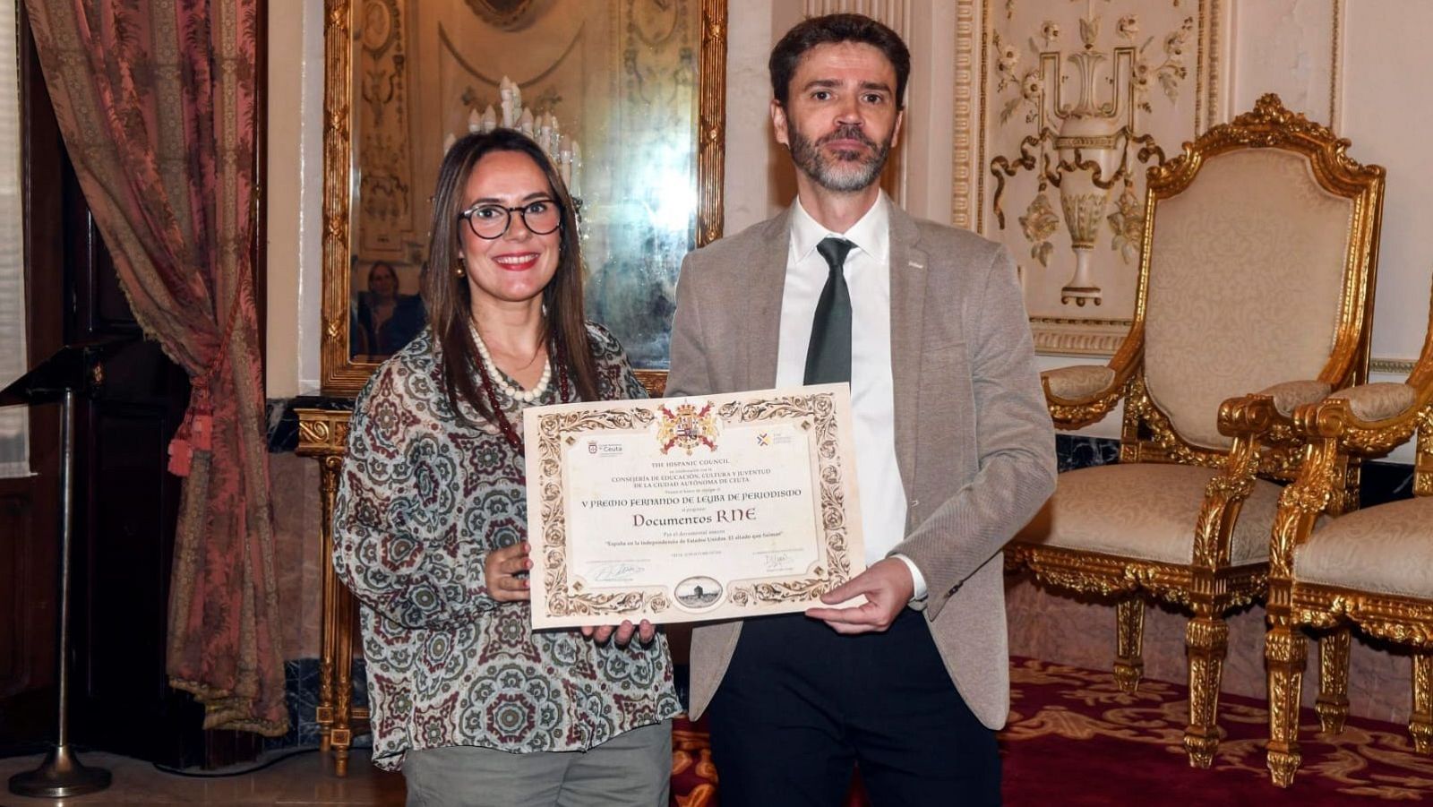 Pilar Orozco y Alfredo Laín posan sonrientes sosteniendo un diploma institucional en un salón señorial.