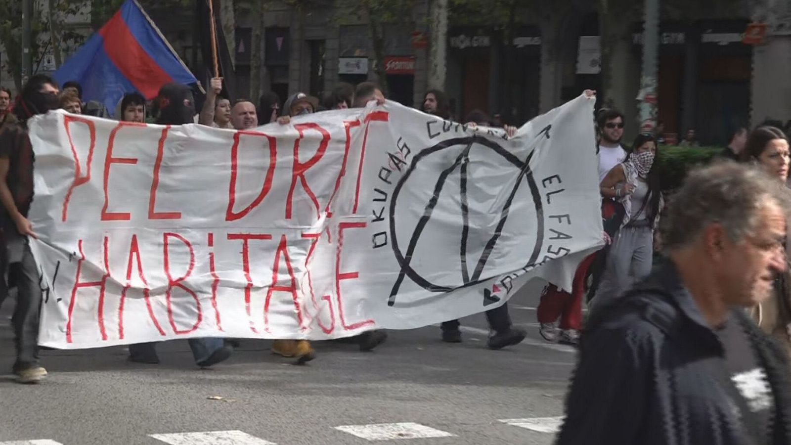 Un grup de manifestants joves desfila per una avinguda urbana sostenint una pancarta amb el lema pel dret a l'habitatge.