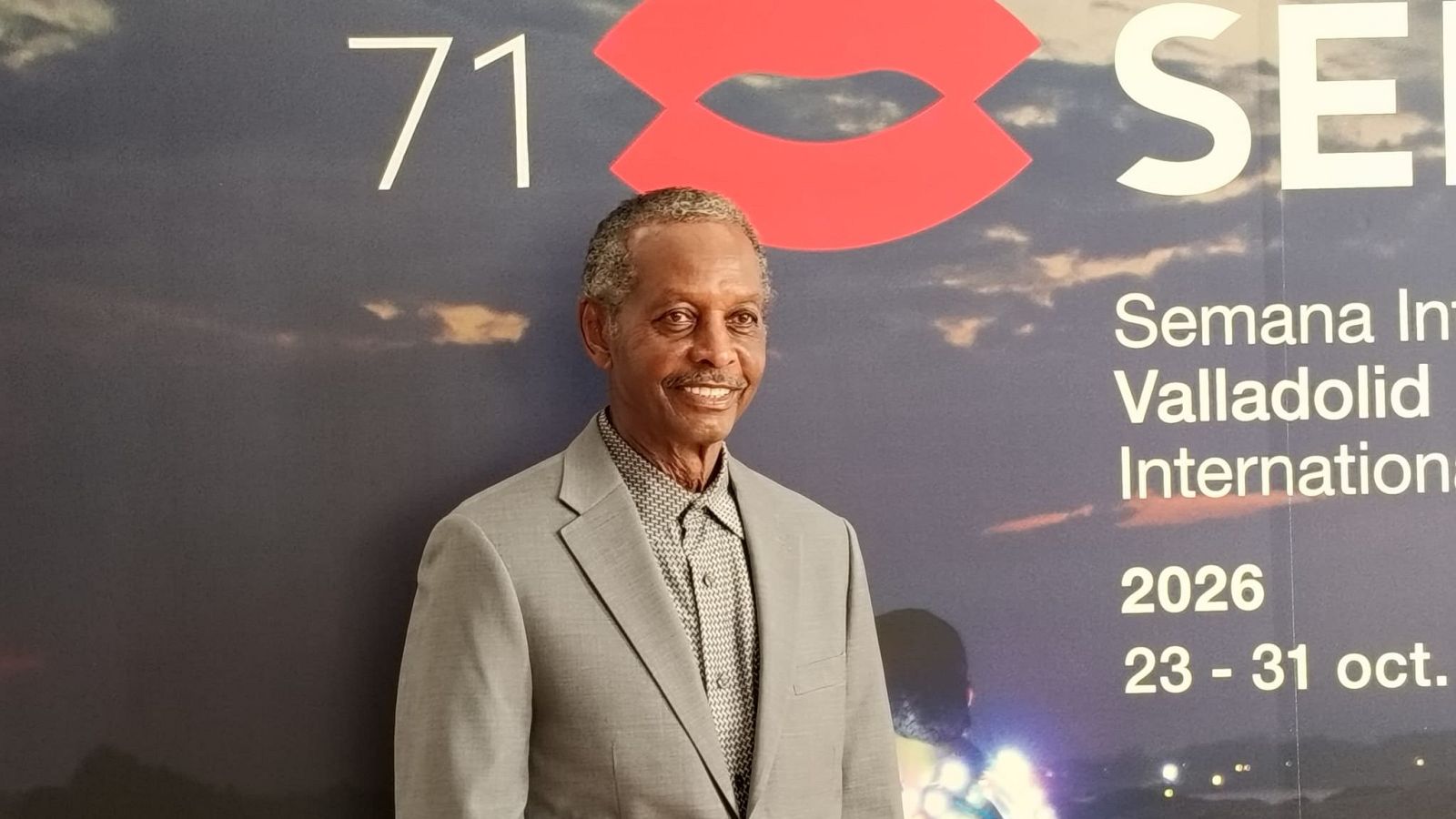 El sonidista Willie D. Burton posa sonriente ante un photocall azul con el logotipo de unos labios rojos y textos del festival.