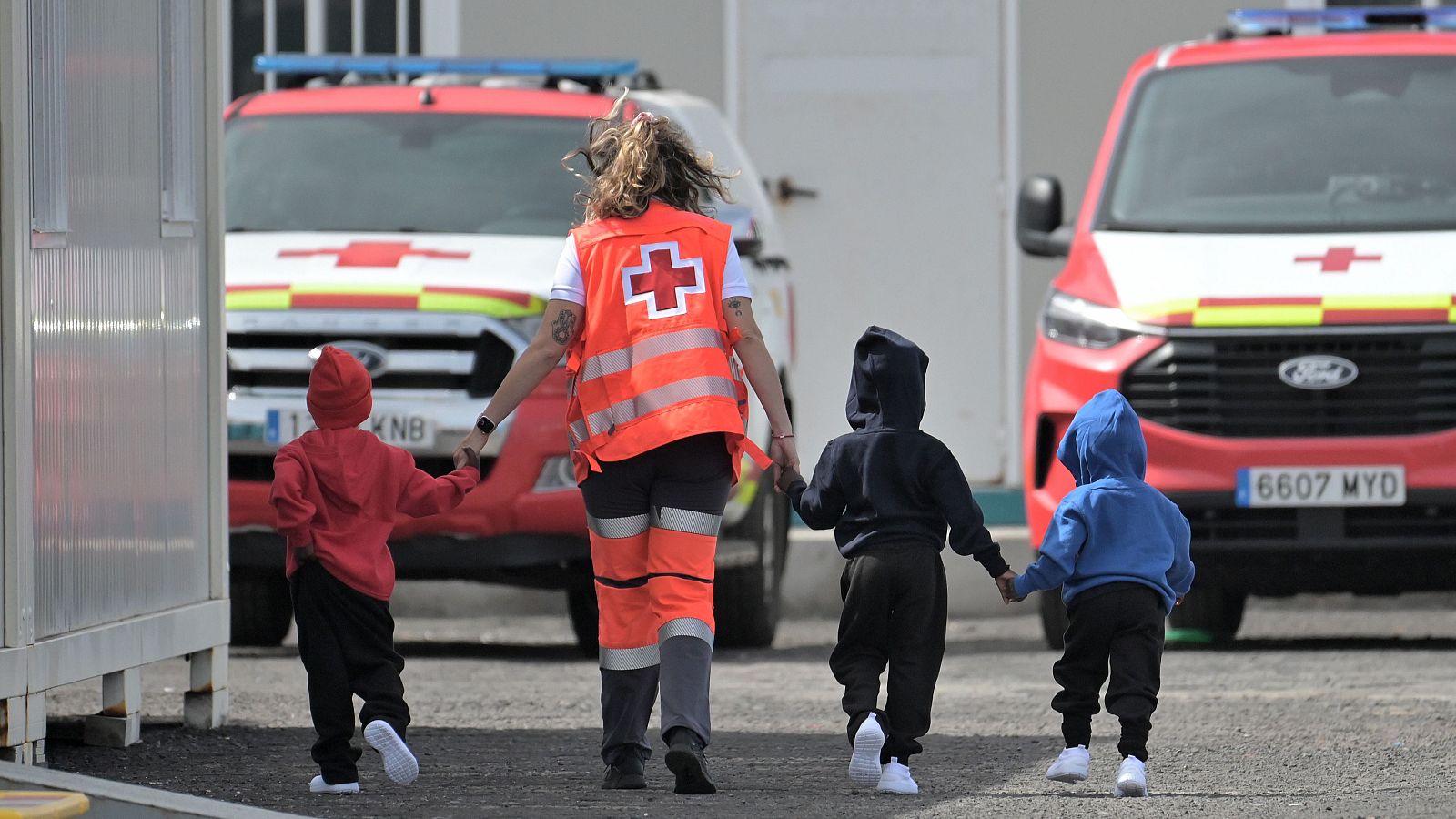 Una miembro de la Cruz Roja acompaña a niños migrantes recién desembarcados de un cayuco de madera en el muelle de La Restinga, El Hierro.