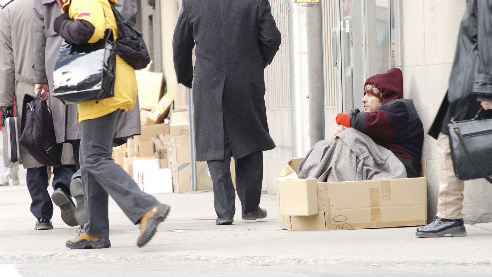 Varias personas pasan por delante de un mendigo