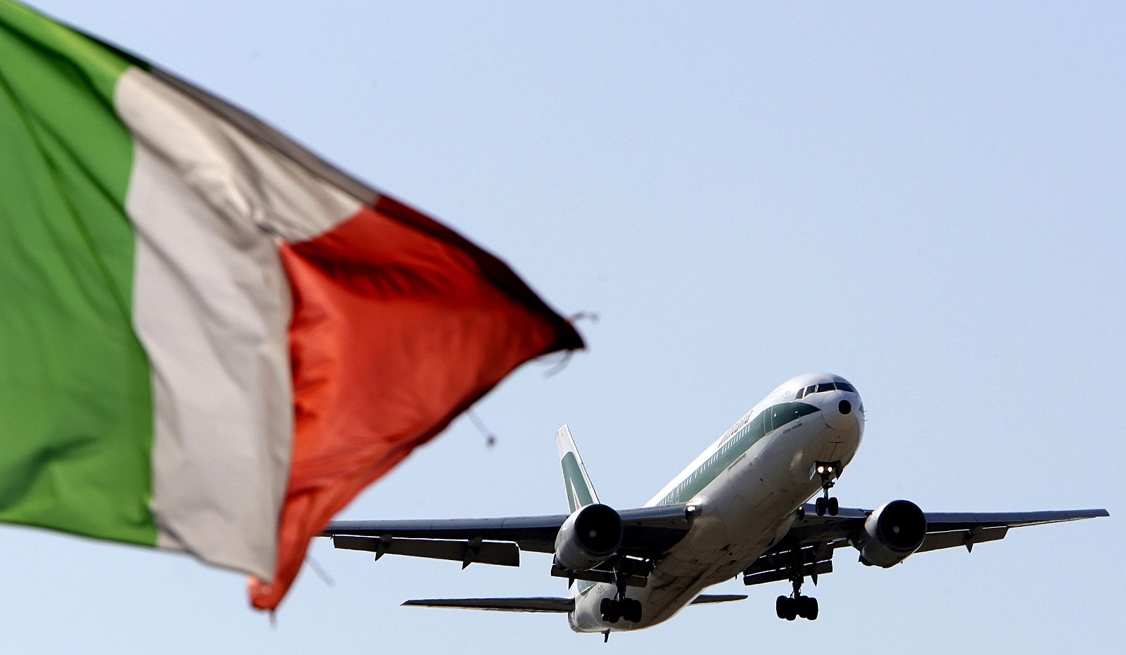 An Alitalia plane approaches to land as an Italian flag is seen at Fiumicino international airport in Rome