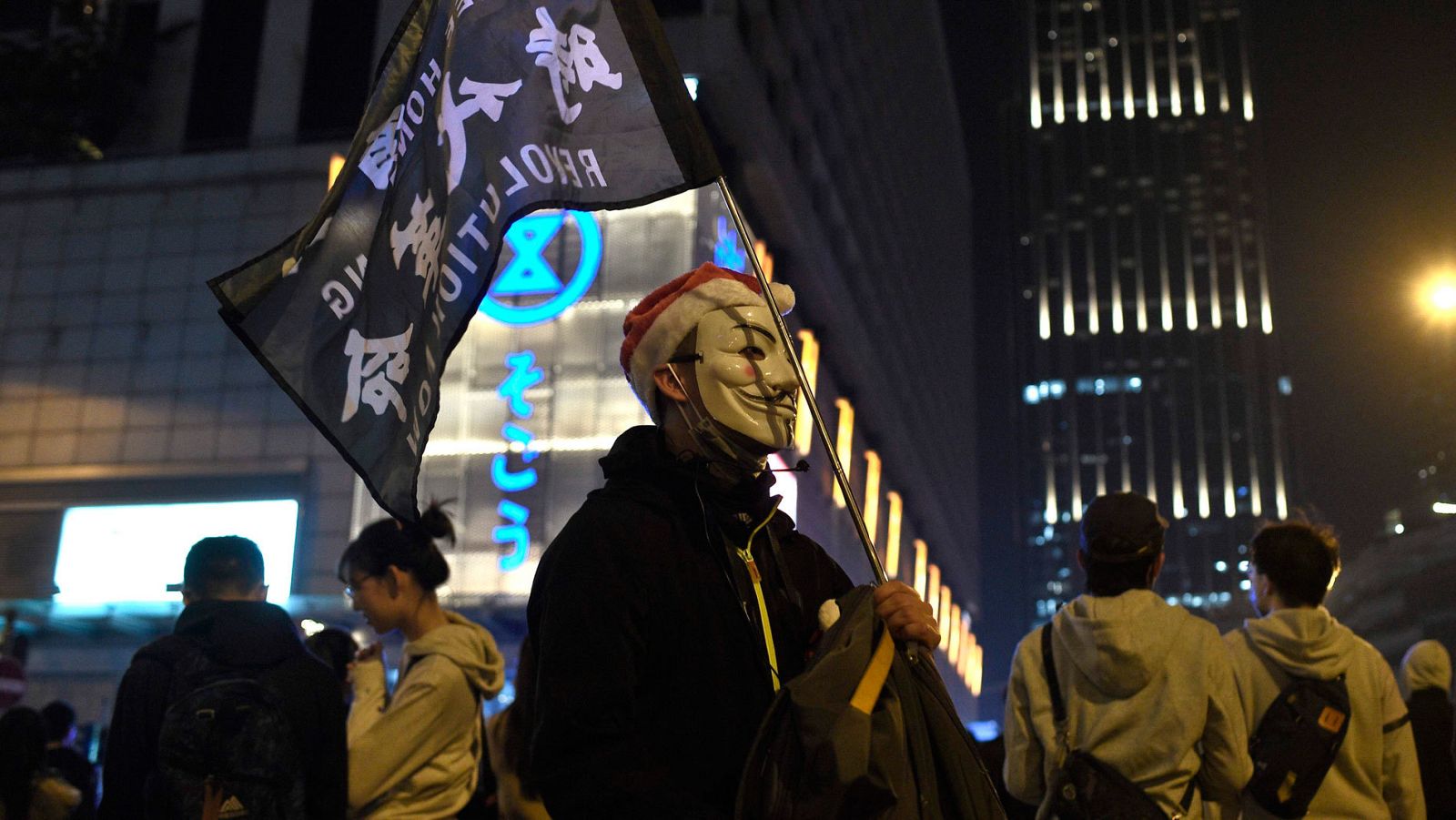 Un manifestante enmascarado con una careta de Guy Fawkes y un gorro de Papá Noel porta una bandera en el distrito de Tsim Sha Tsui en Hong Kong