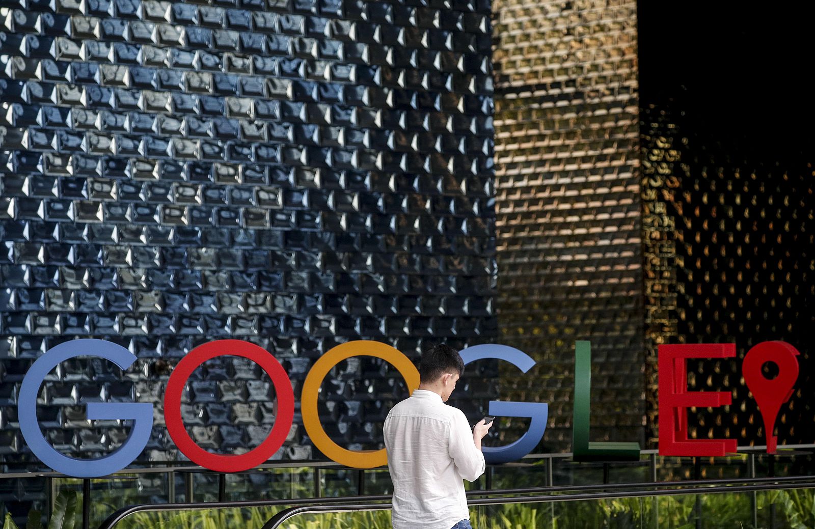 Singapur. Hombre usando su teléfono móvil mientras camina ante el logo de Google en Singapur