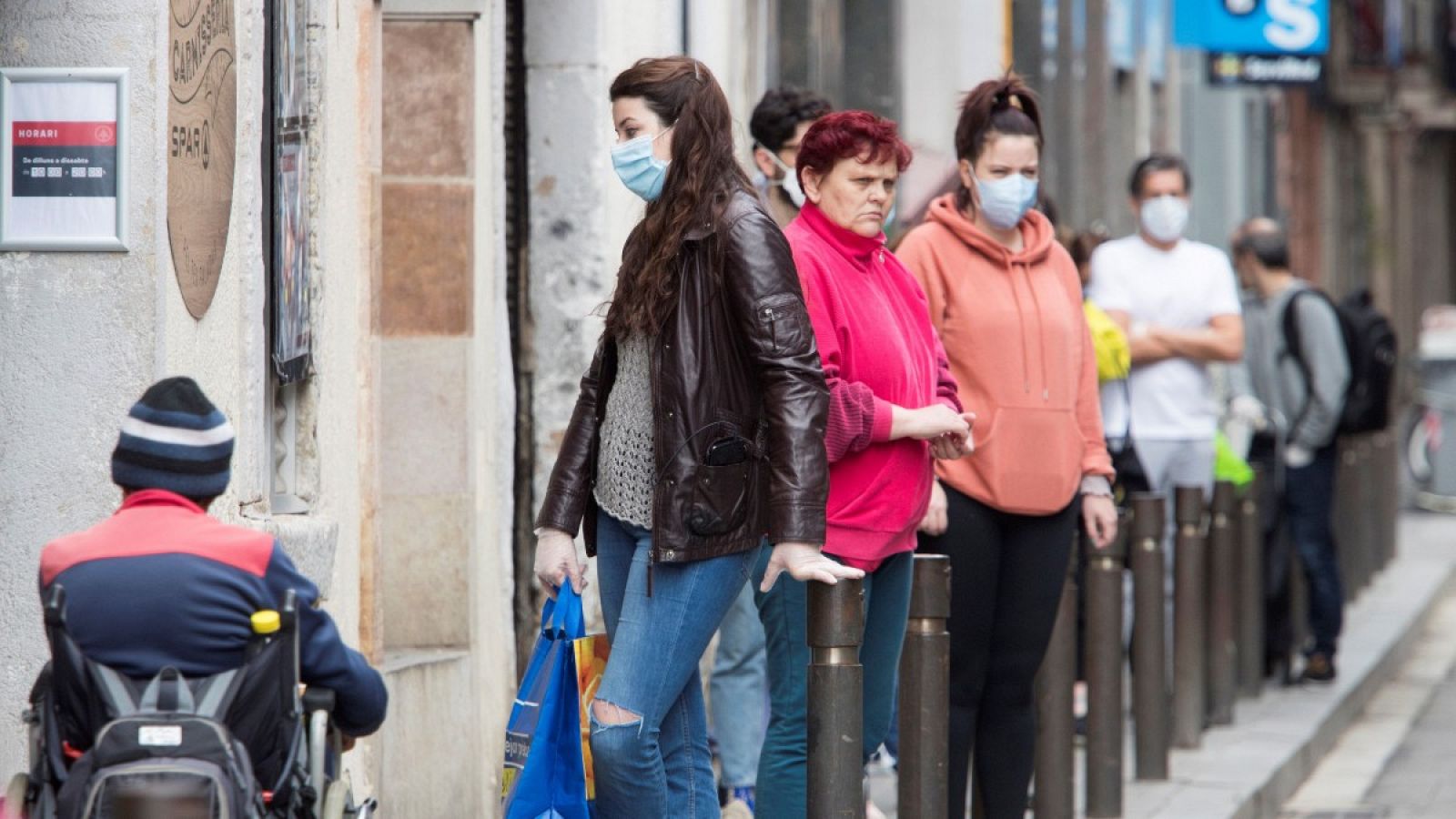 Varios vecinos con mascarilla hacen cola para entrar en un comercio