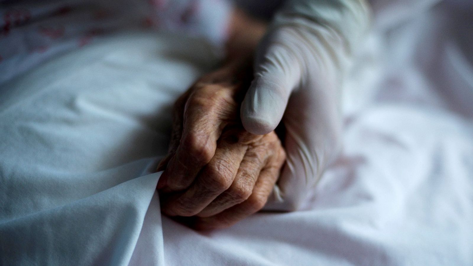 Imagen de una trabajadora de una residencia de mayores sujetando la mano de una residente