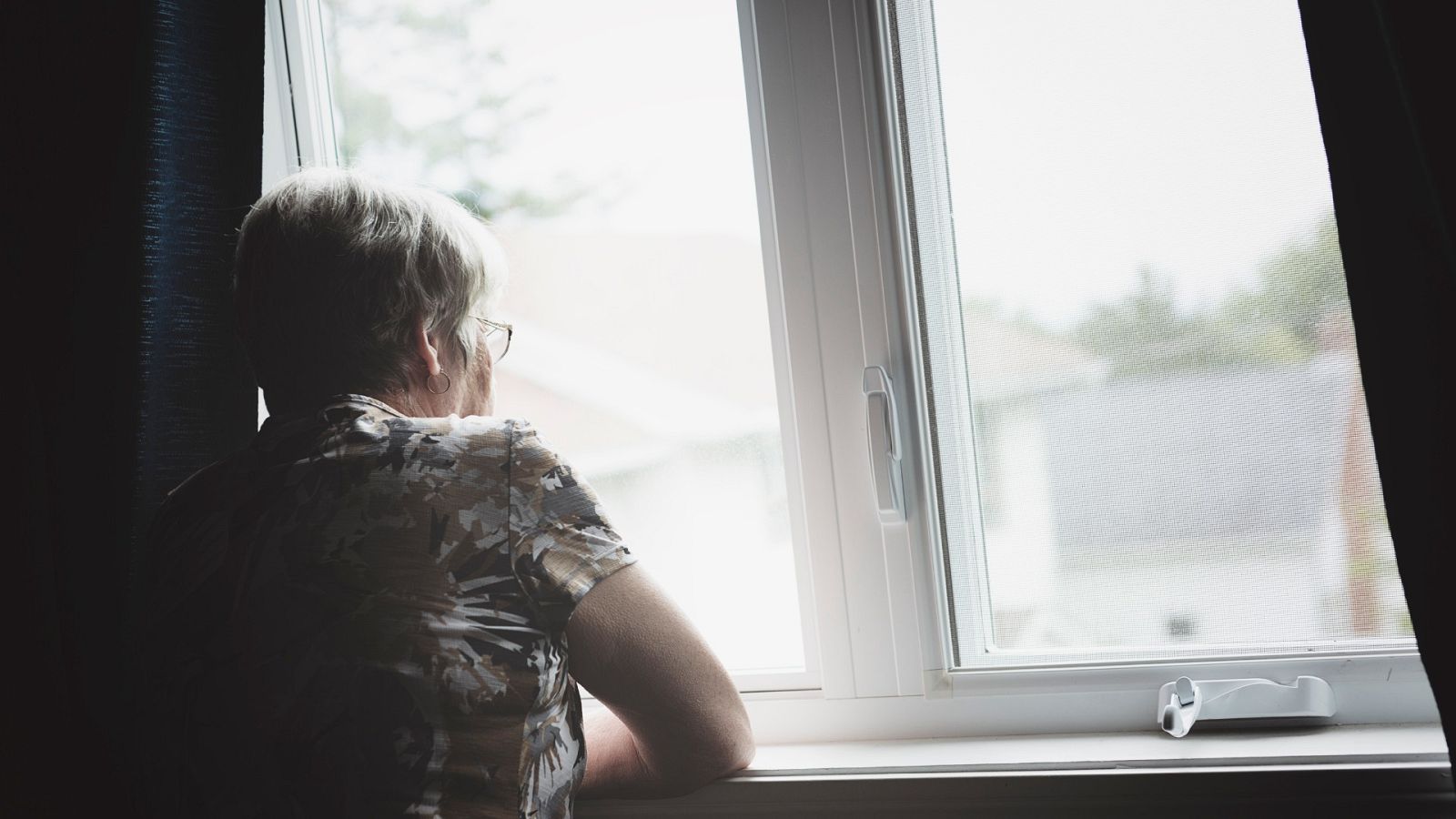 Una mujer se asoma por la ventana de su apartamento