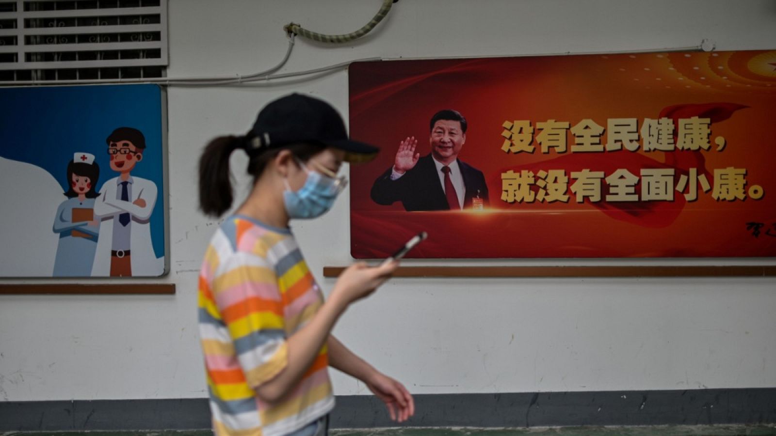 Una mujer con mascarilla pasando por delante de un cartel con una imagen del presidente Xi Jinping.