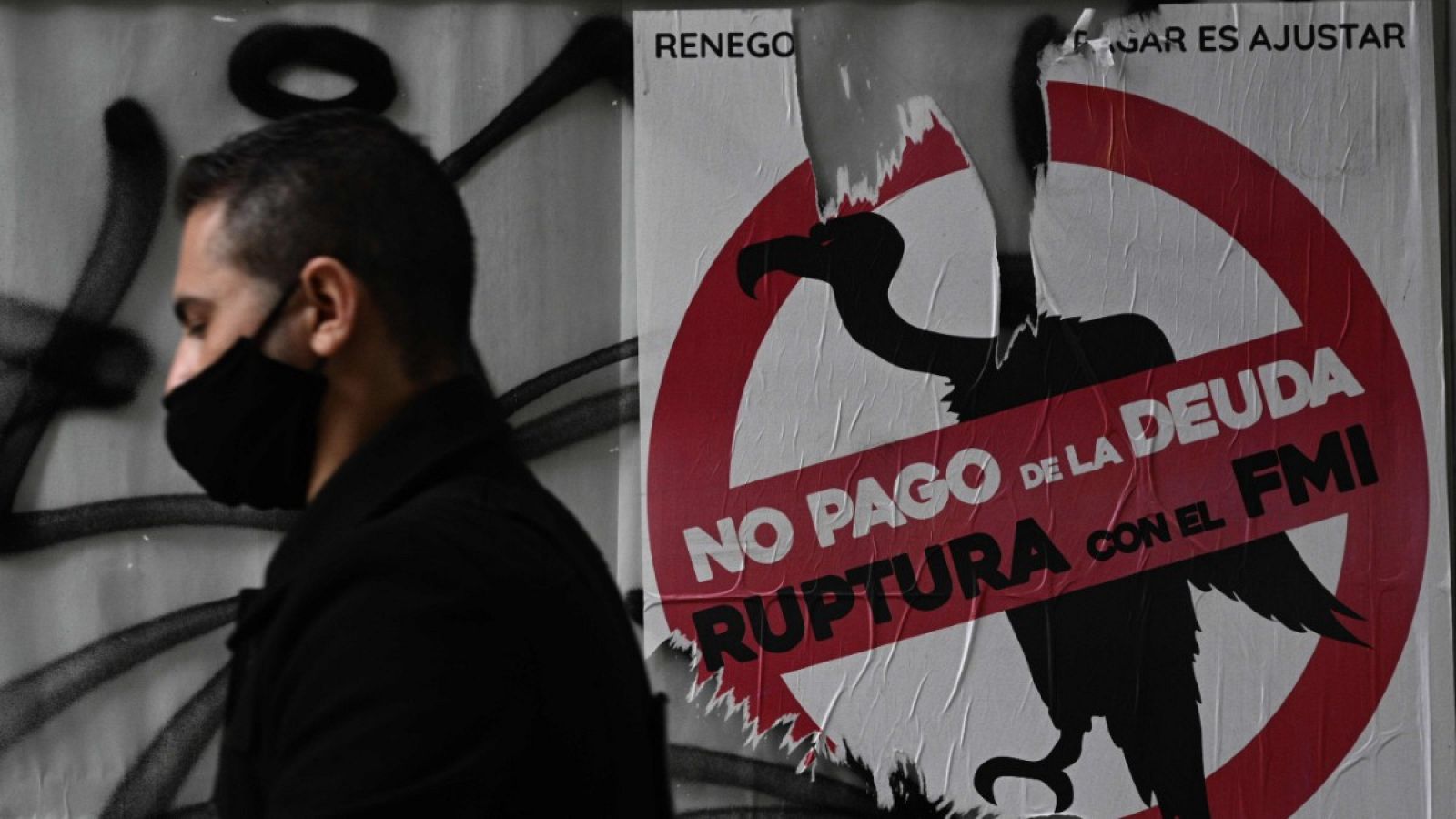 Un hombre pasando frente a un cartel con un contra el Fondo Monetario Internacional.