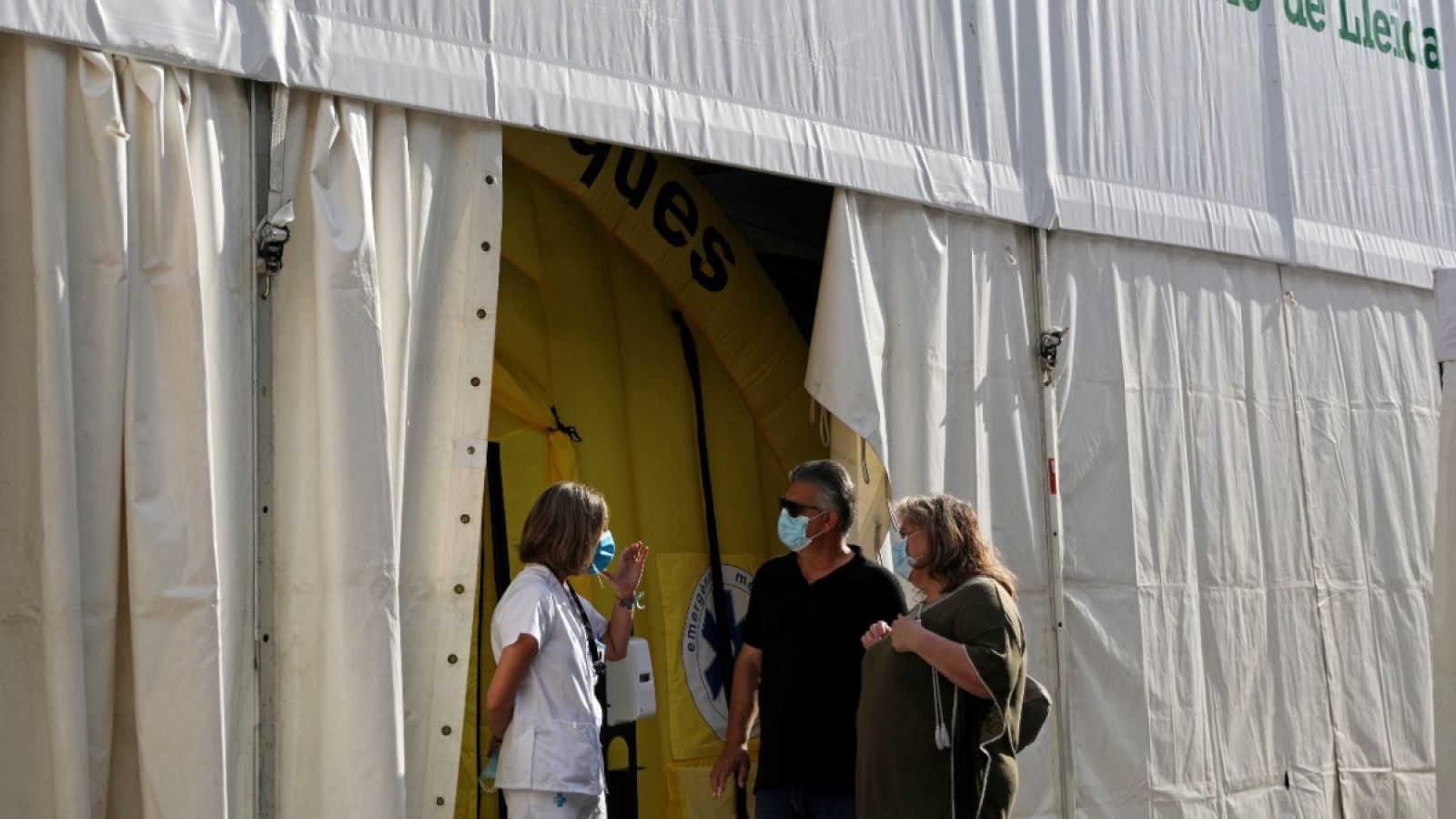 Una sanitaria habla con dos personas a la salida de un hospital de campaña en Lleida