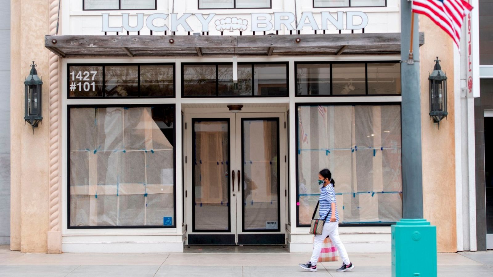 Una viandante con mascarilla pasa por delante de una tienda cerrada en Santa Mónica, California