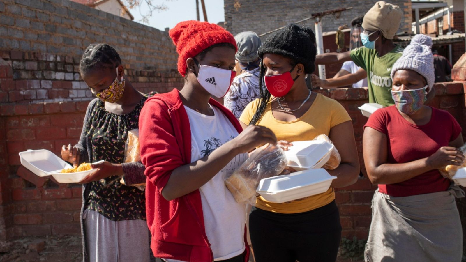 Mujeres con mascarilla recibiendo pan y alimentos en Johannesburgo, Sudáfrica.