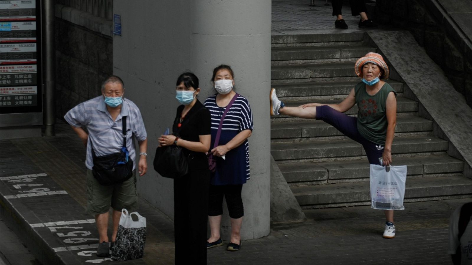 Varias personas con mascarilla esperando al autobús en una parada de Pekín.