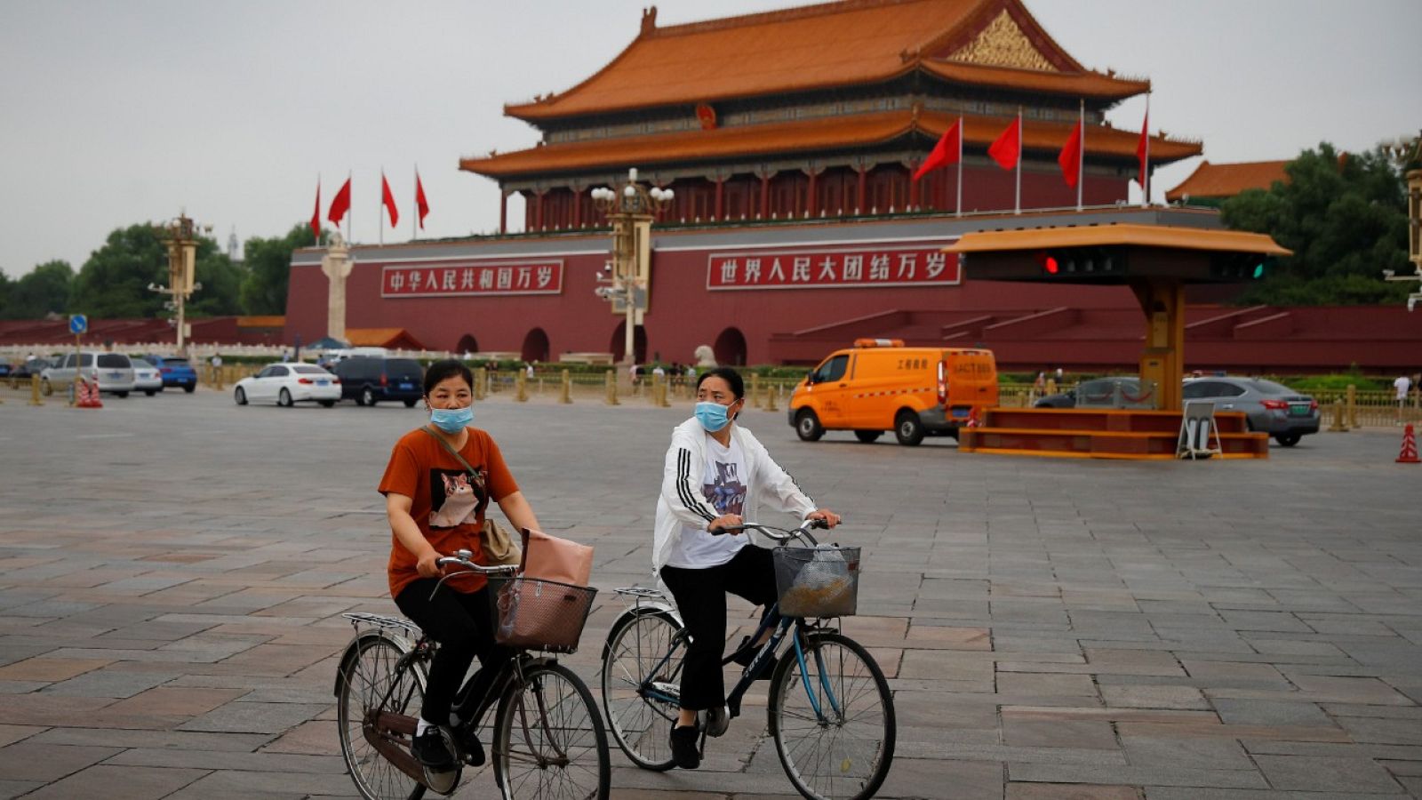 Dos mujeres con mascarilla montando en bicicleta por la plaza de Tiananmen en Pekín, China.