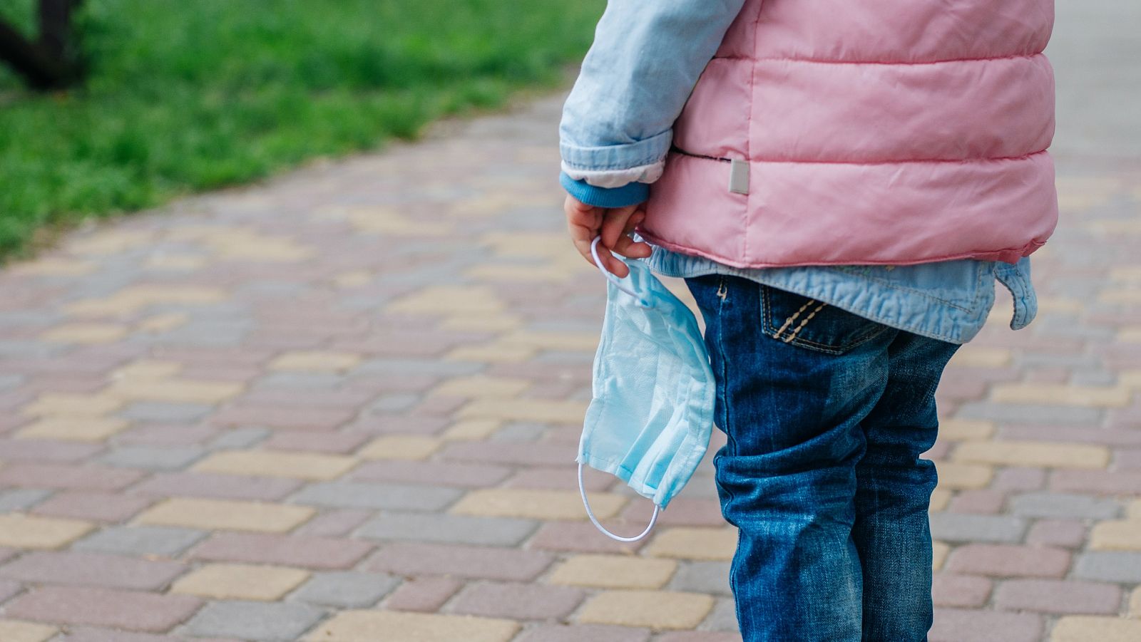 Una niña sostiene una mascarilla mientras camina por la calle