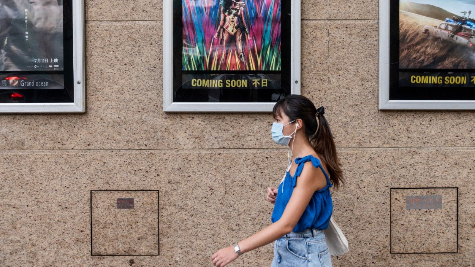 Una mujer con mascarilla pasa por delante de un cine en Hong Kong