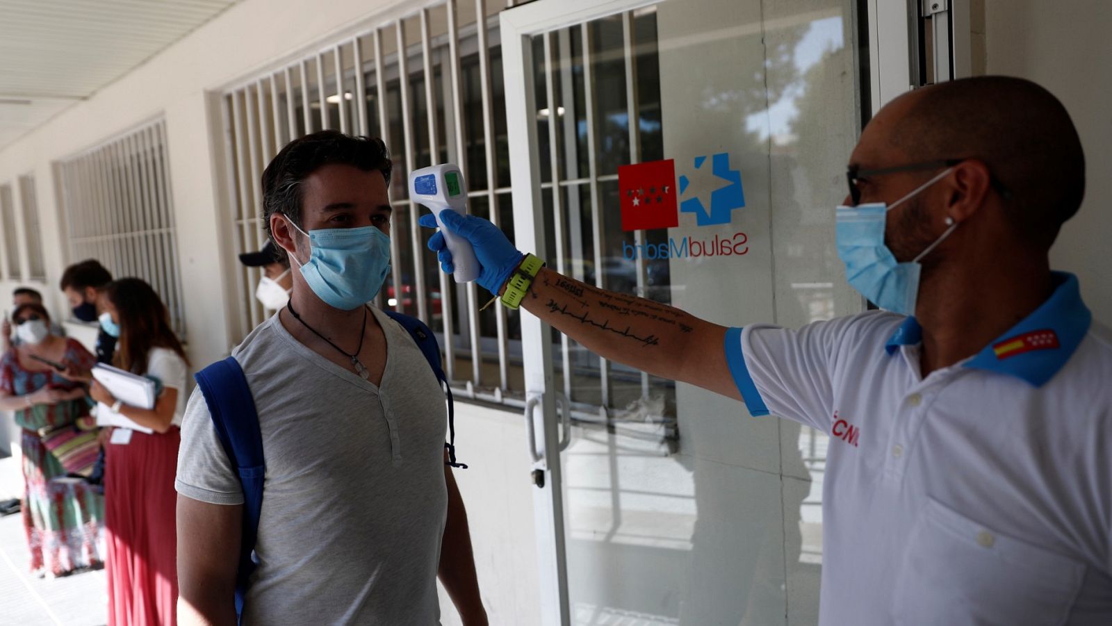 Un sanitario toma la temperatura a una persona que espera para realizarse una prueba de PCR en Madrid