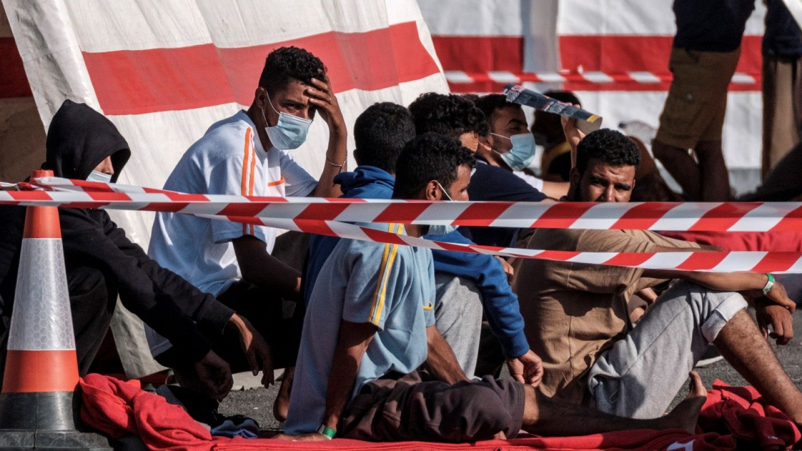 Imagen de varios inmigrantes con mascarillas sentados en el muelle grancanario de Arguineguín.