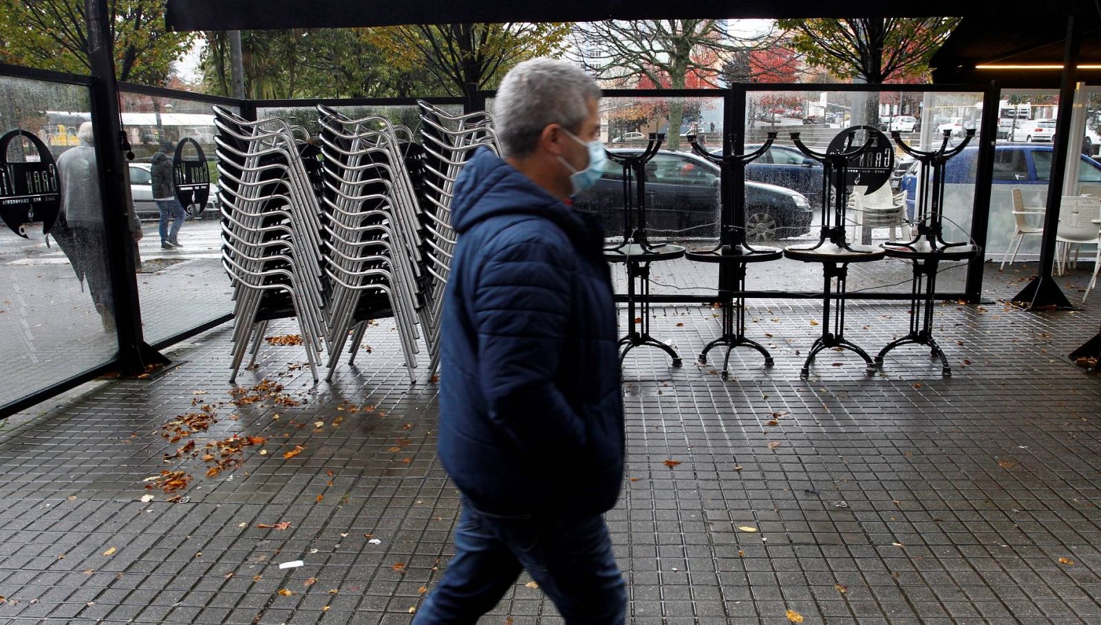 Un hombre camina al lado de las sillas y las mesas apiladas en una terraza cerrada en Galicia