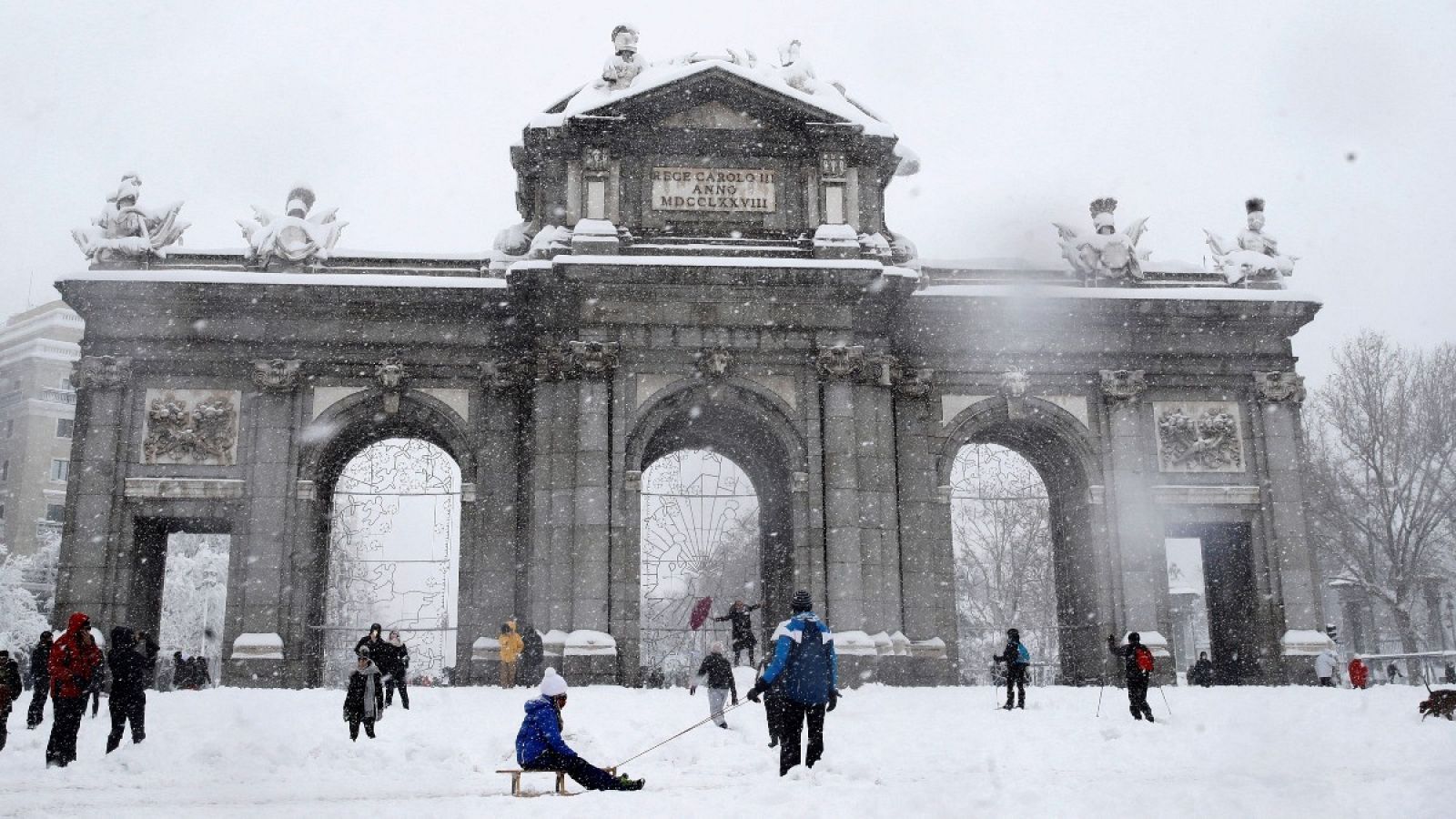 Varias personas caminan junto a la Puerta de Alcalá de Madrid, este sábado