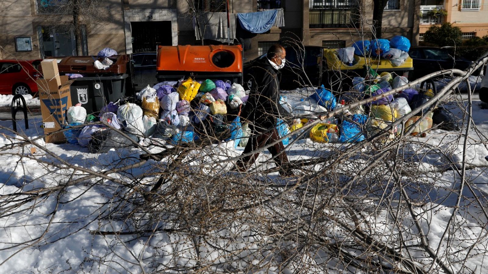 Un hombre pasea por la nieve entre las ramas de un árbol caído y bolsas de basura en Madrid