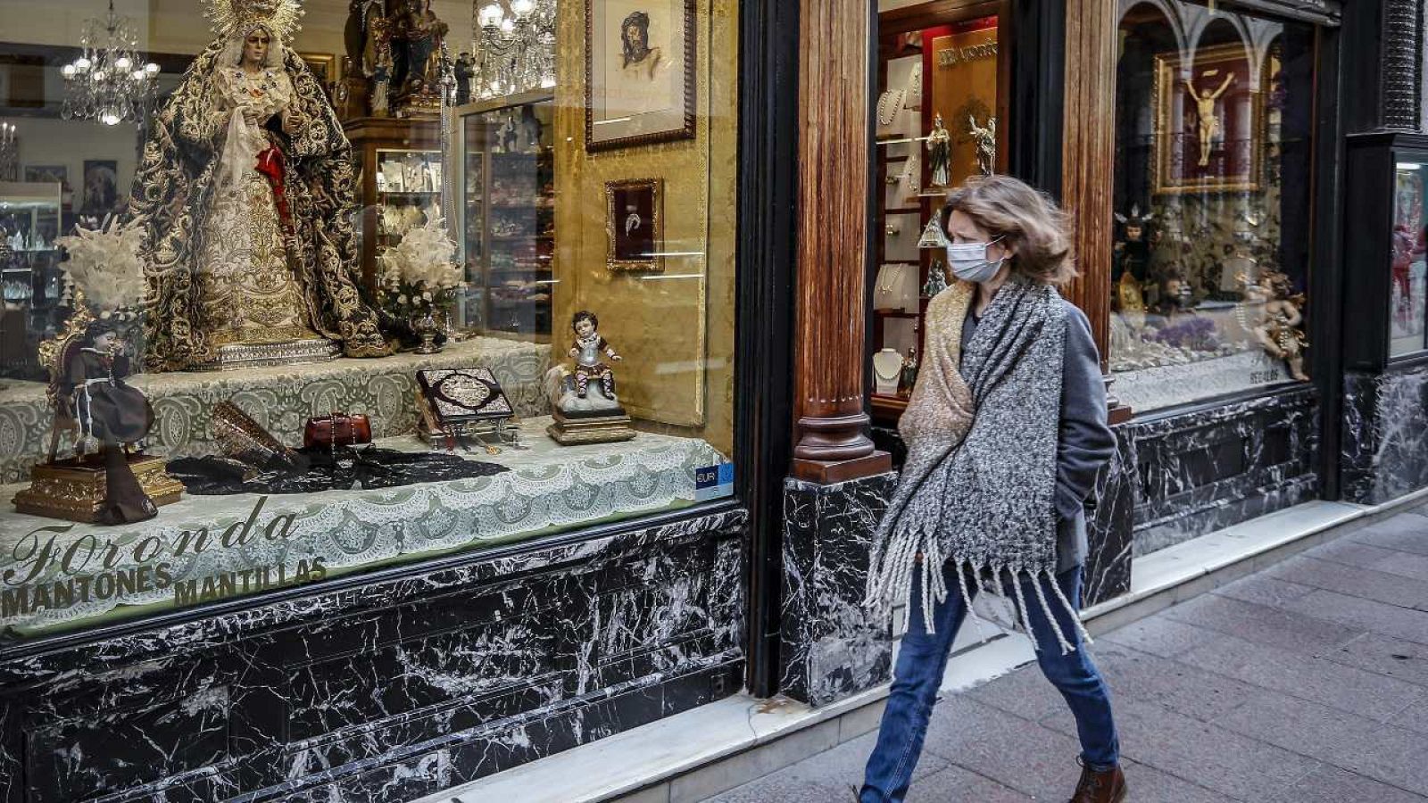 Una mujer pasa junto a un escaparate decorado con imágenes de Semana Santa en Sevilla.