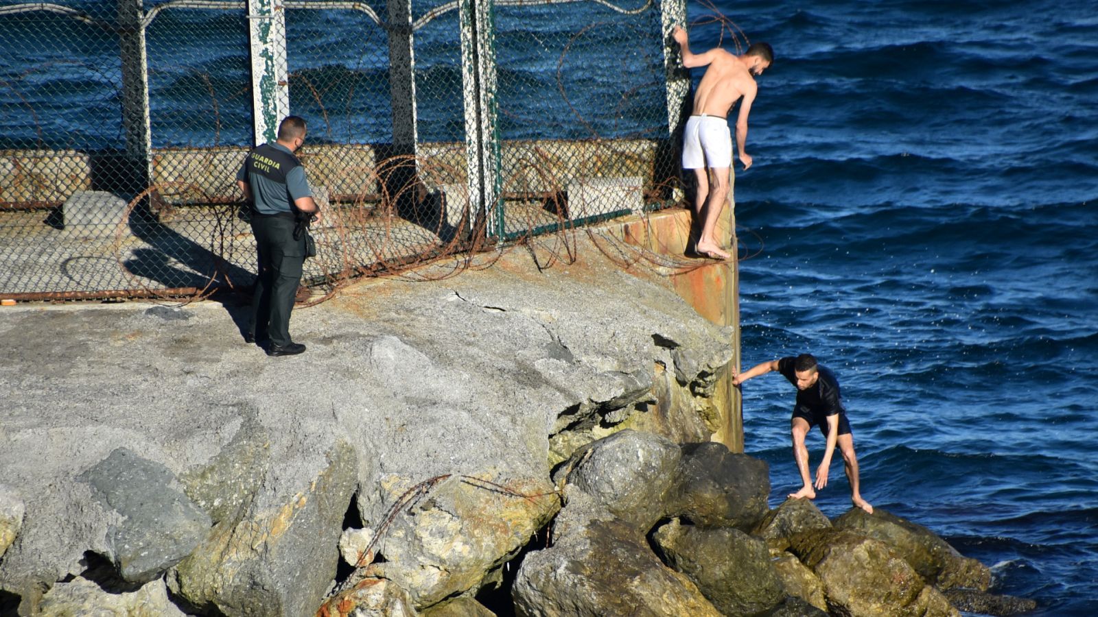 Dos migrantes tratan de cruzar la frontera en presencia de un guardia civil