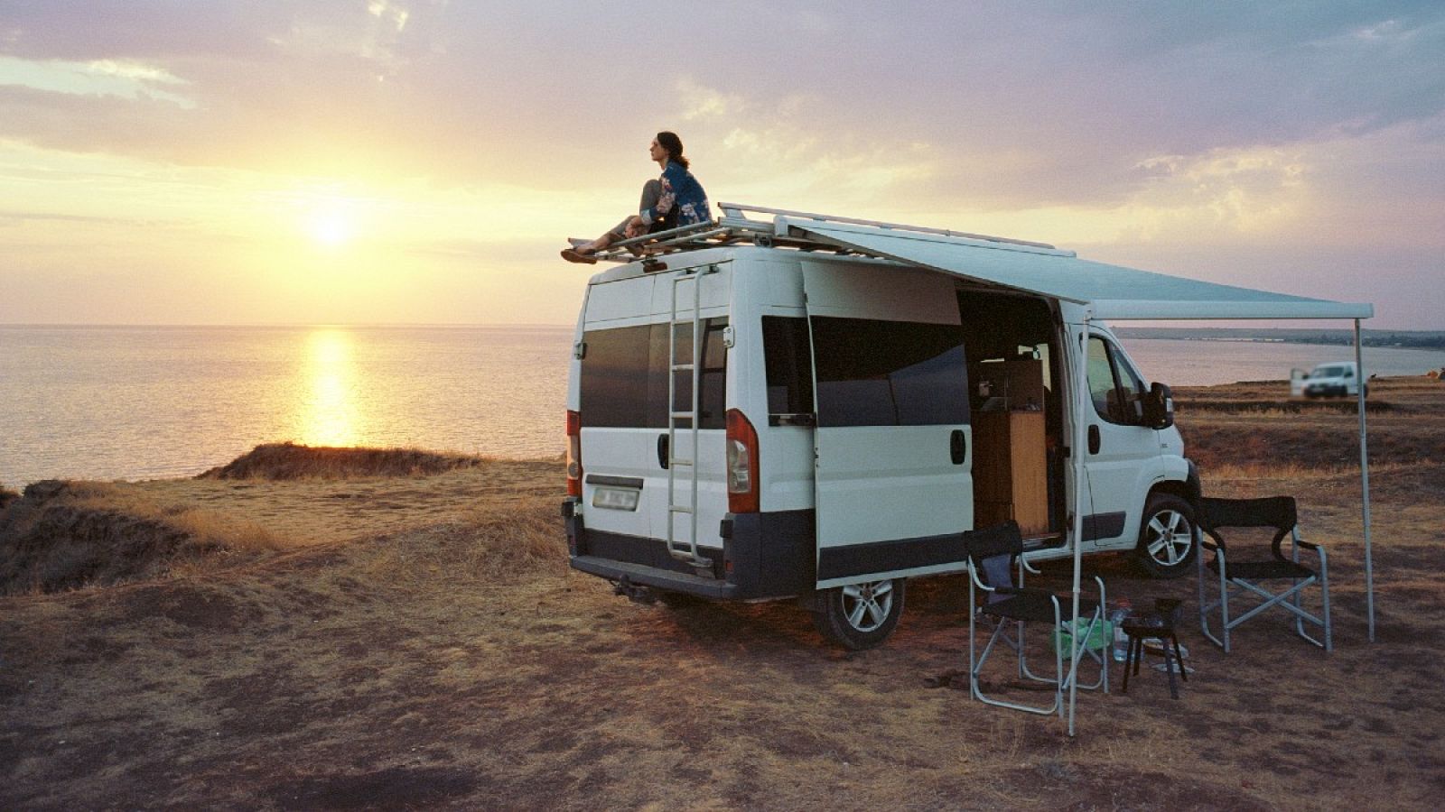 Mujer sentada en el techo de una 'camper' cerca del mar