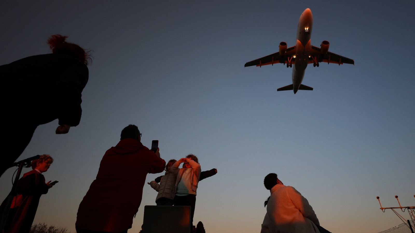 Un grupo de personas se fotografía al tiempo que un avión aterriza en el aeropuerto de Barcelona
