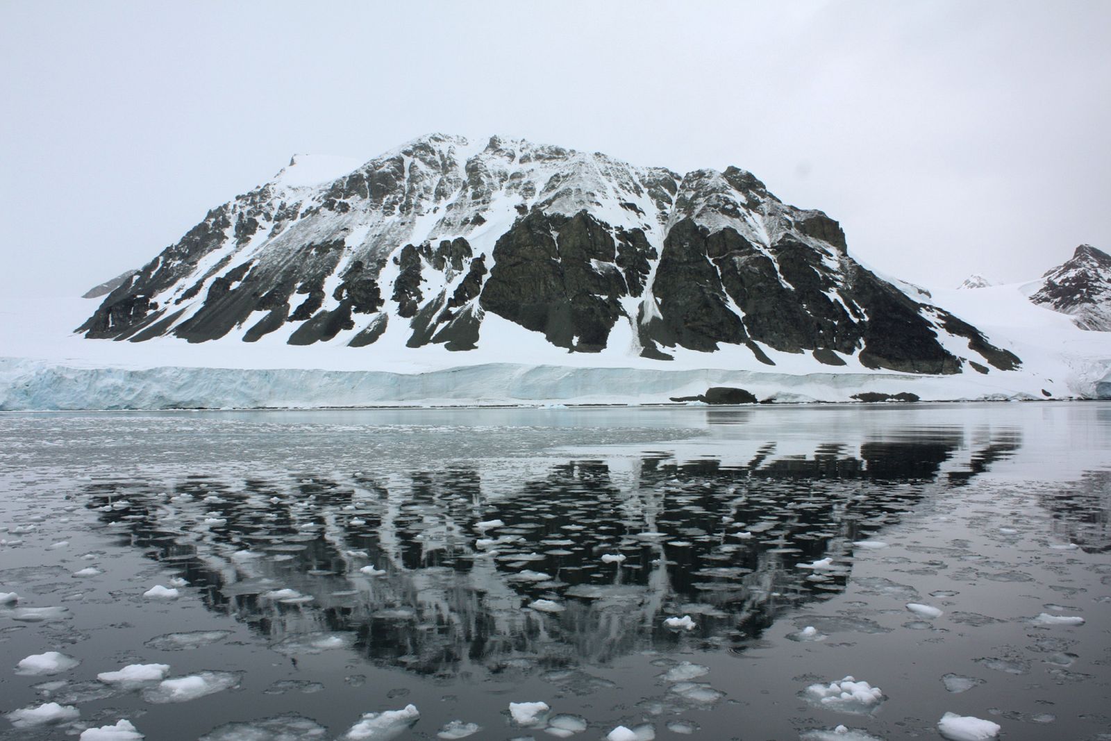 Mountain is reflected in a bay that used to be covered by the Sheldon glacier on the Antarctic peninsula