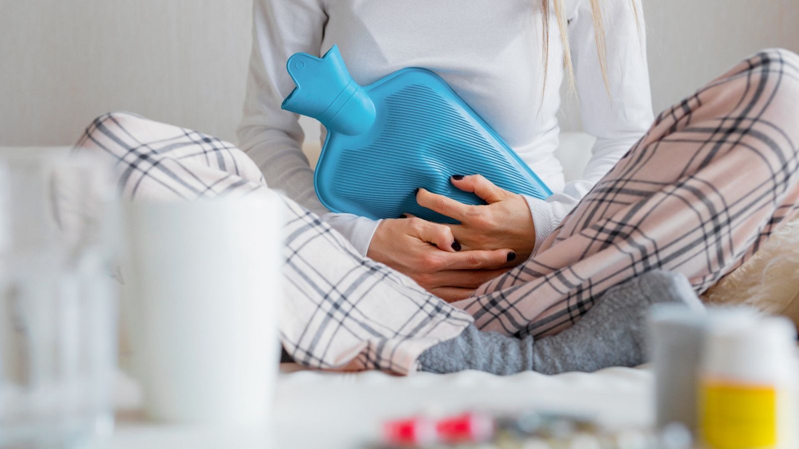 Una mujer aguanta el dolor menstrual con antiinflamatorios y una bolsa de calor
