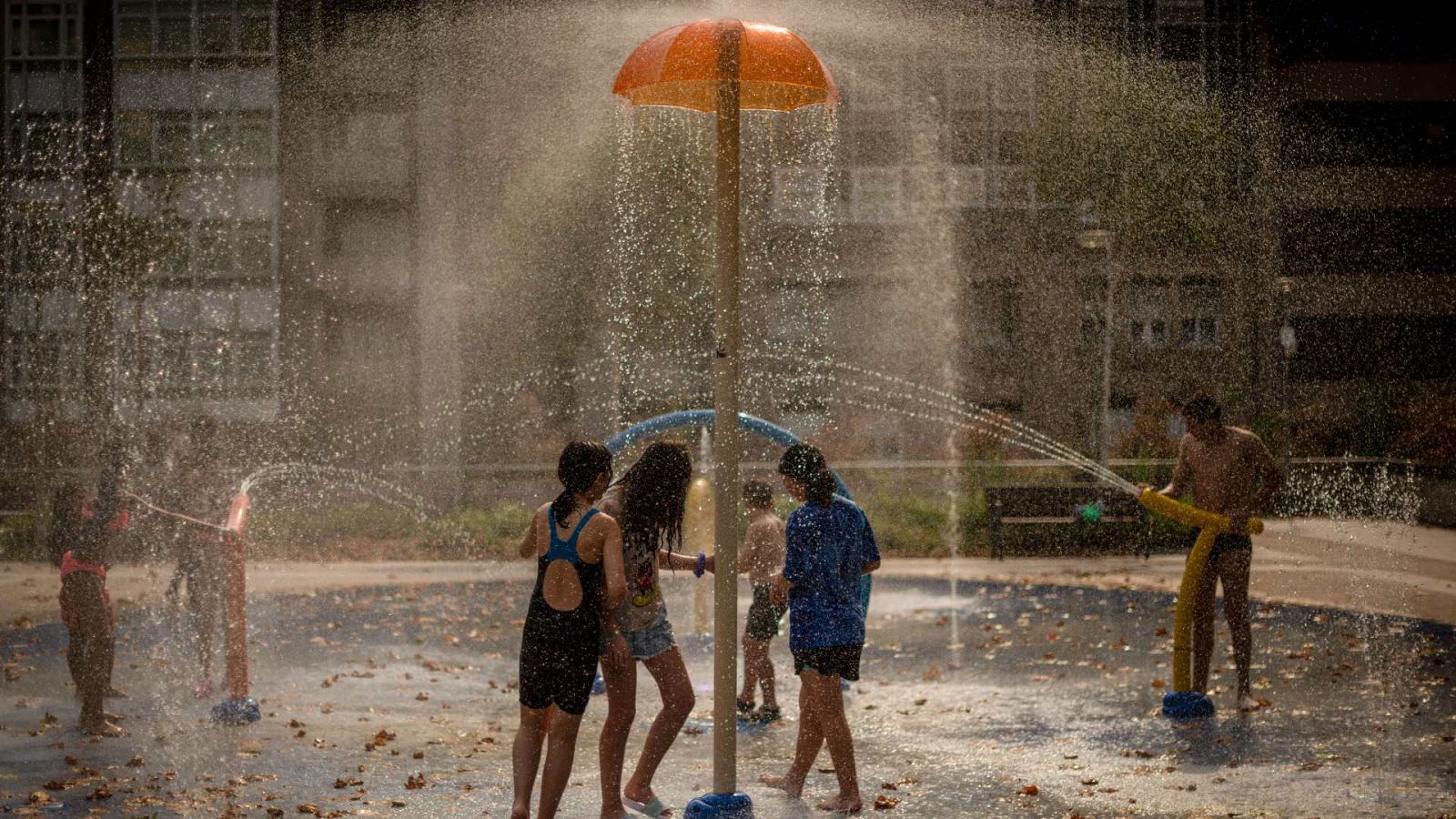 Varios niños se refrescan con una fuente de un parque público