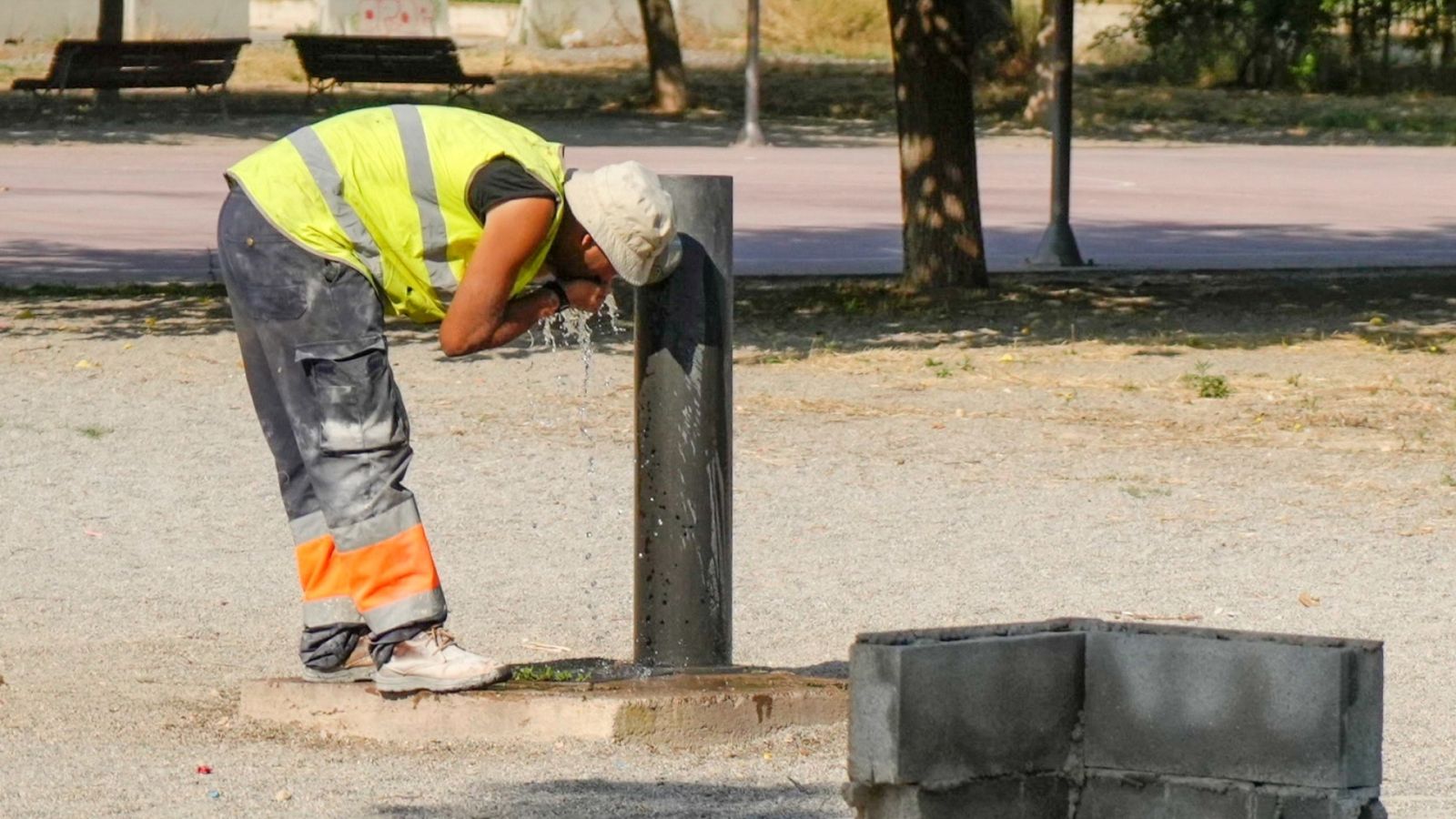 Un trabajador se refresca en un fuente de un parque de Lleida