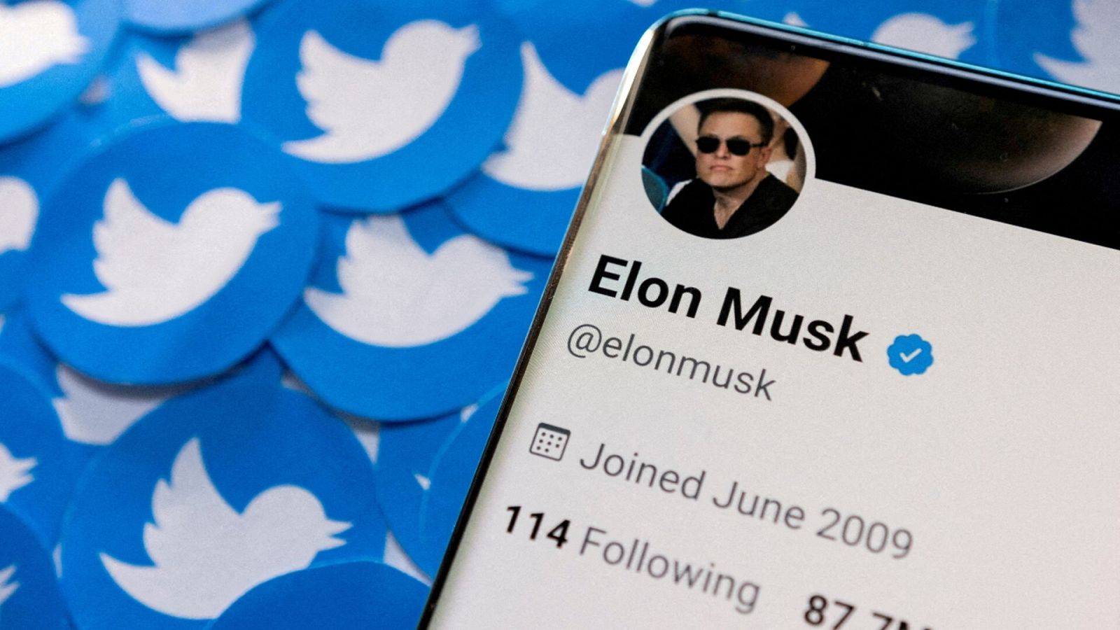 El perfil de Twitter de Elon Musk en un teléfono móvil junto a logotipos impresos de la empresa tecnológica.