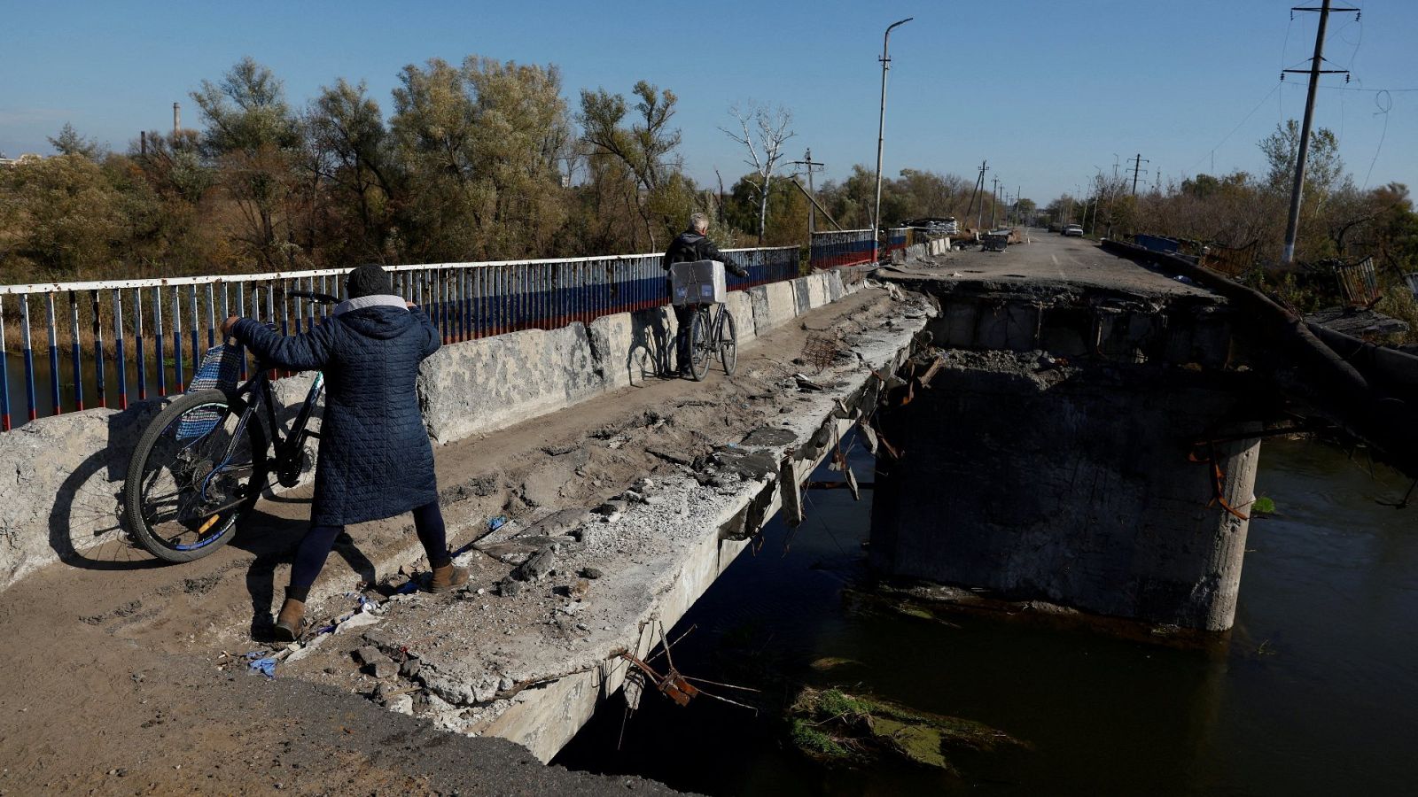 Una mujer empuja su bicicleta a lo largo de un puente destruido en Kupiansk